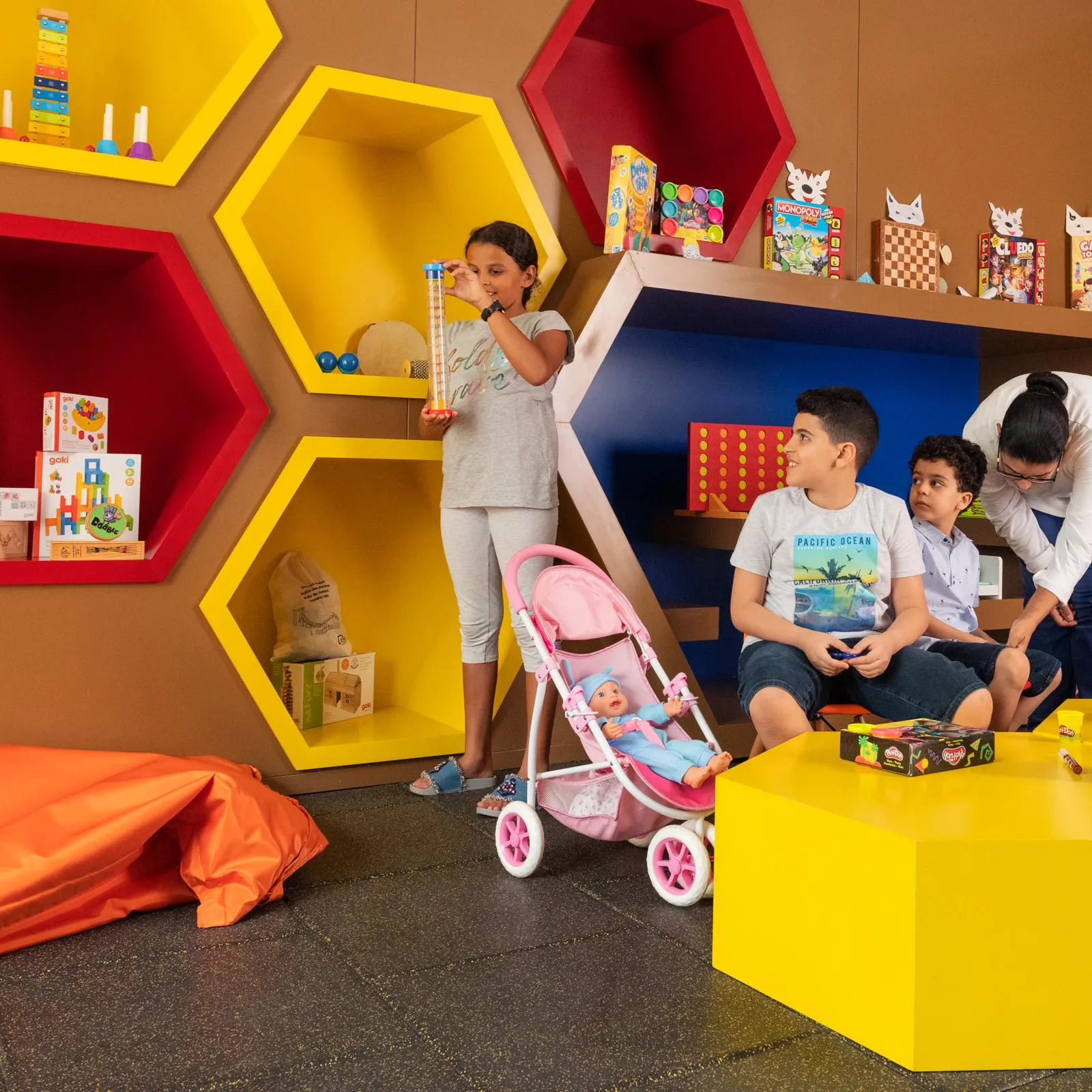 Children playing in a colorful room filled with toys and hexagonal shelves