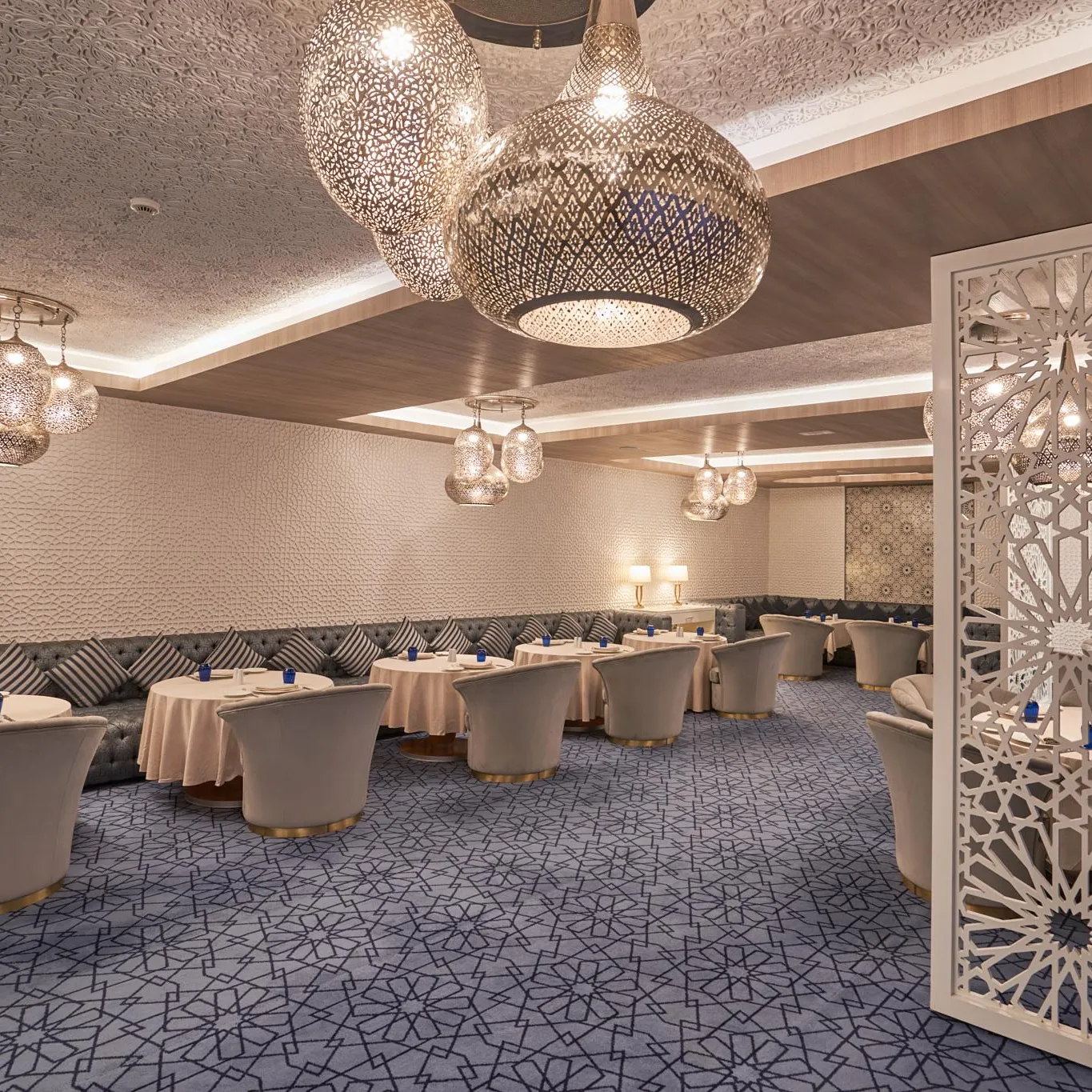 Elegant restaurant with round tables, matching chairs, metal light fixtures, and geometric patterns on the walls and floor.