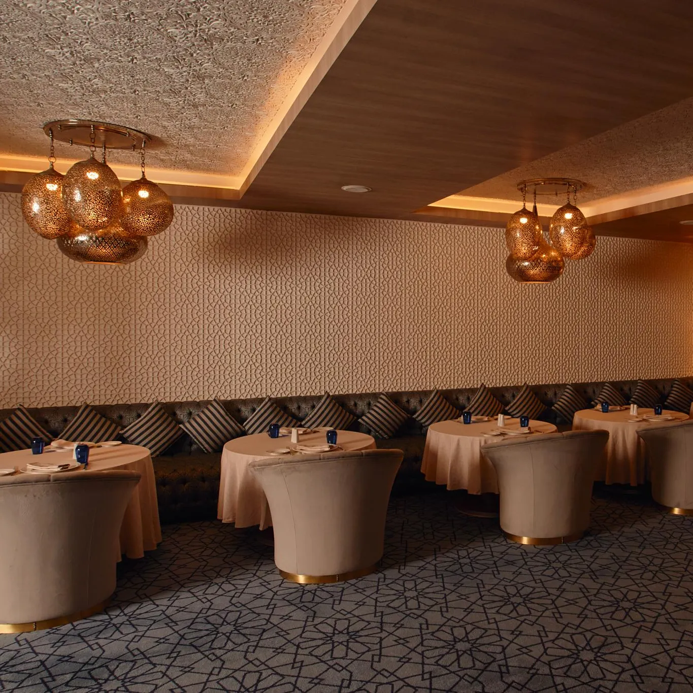 Elegant restaurant room with round tables covered in beige tablecloths, banquettes, and suspended light fixtures