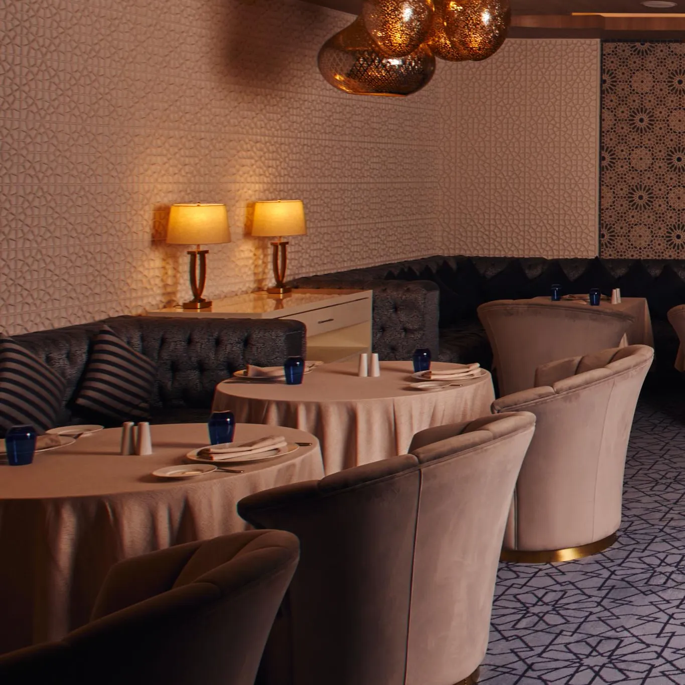 An elegant restaurant with round tables covered in pink tablecloths, padded chairs, and hanging light fixtures.