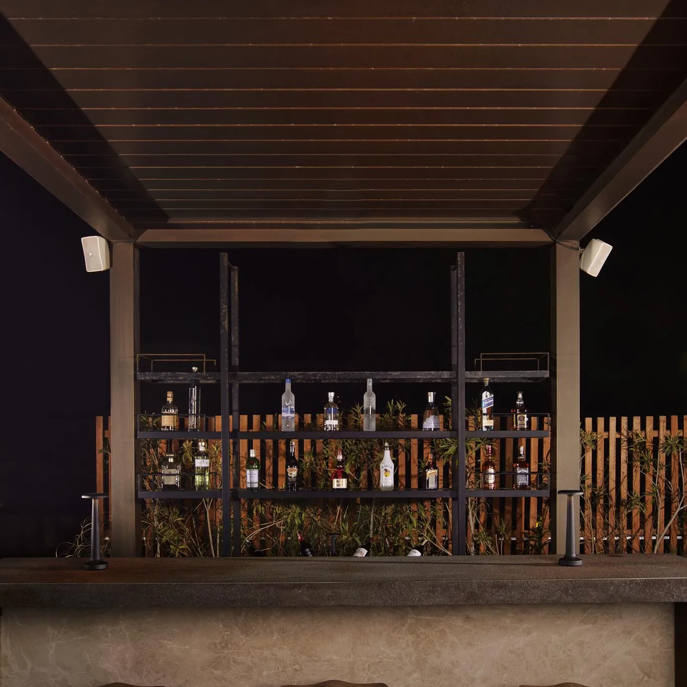 Bar with bottle shelves and three wooden stools in front of a stone wall