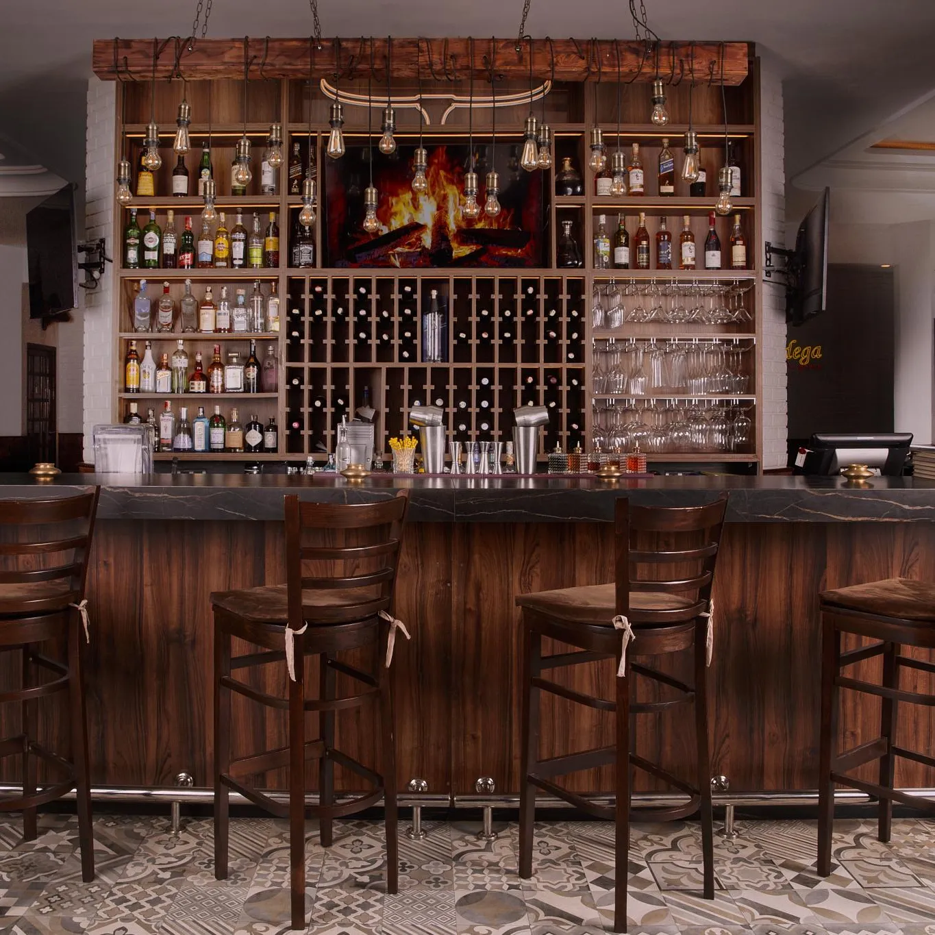 A wooden bar with stools lined up in front, shelves filled with bottles and glasses, and a floor with geometric patterns.