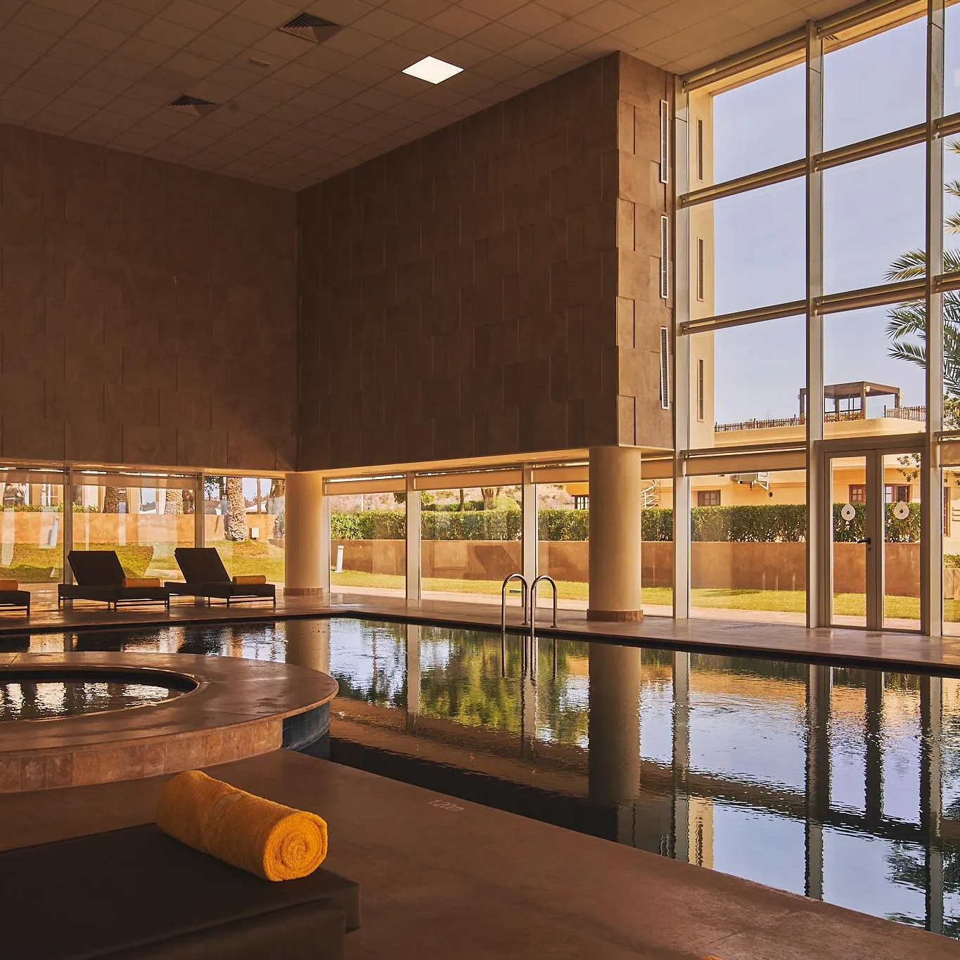 Indoor pool with sun loungers and towels, surrounded by large windows and stone walls