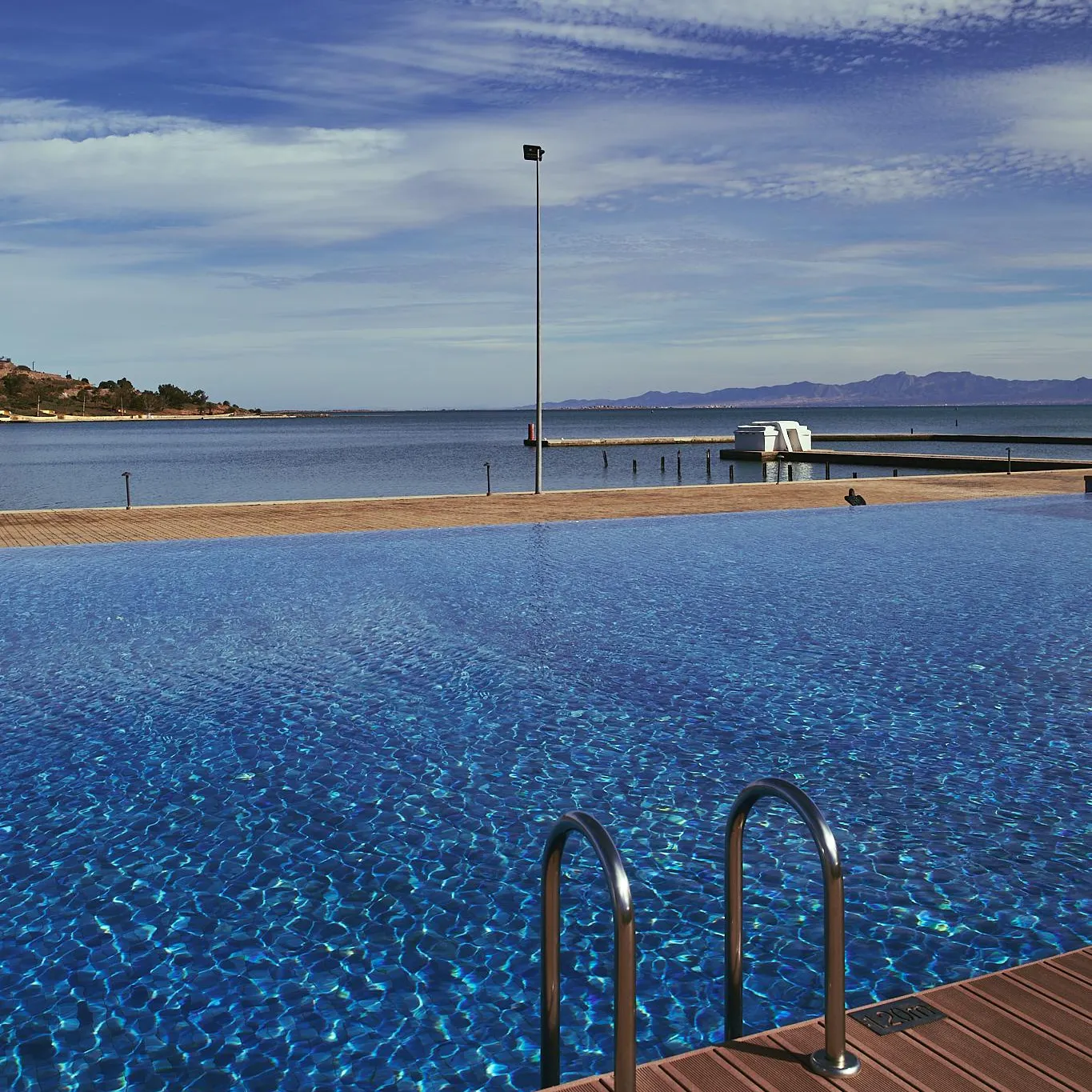 Overflow pool with a view of the sea and distant mountains under a partly cloudy sky