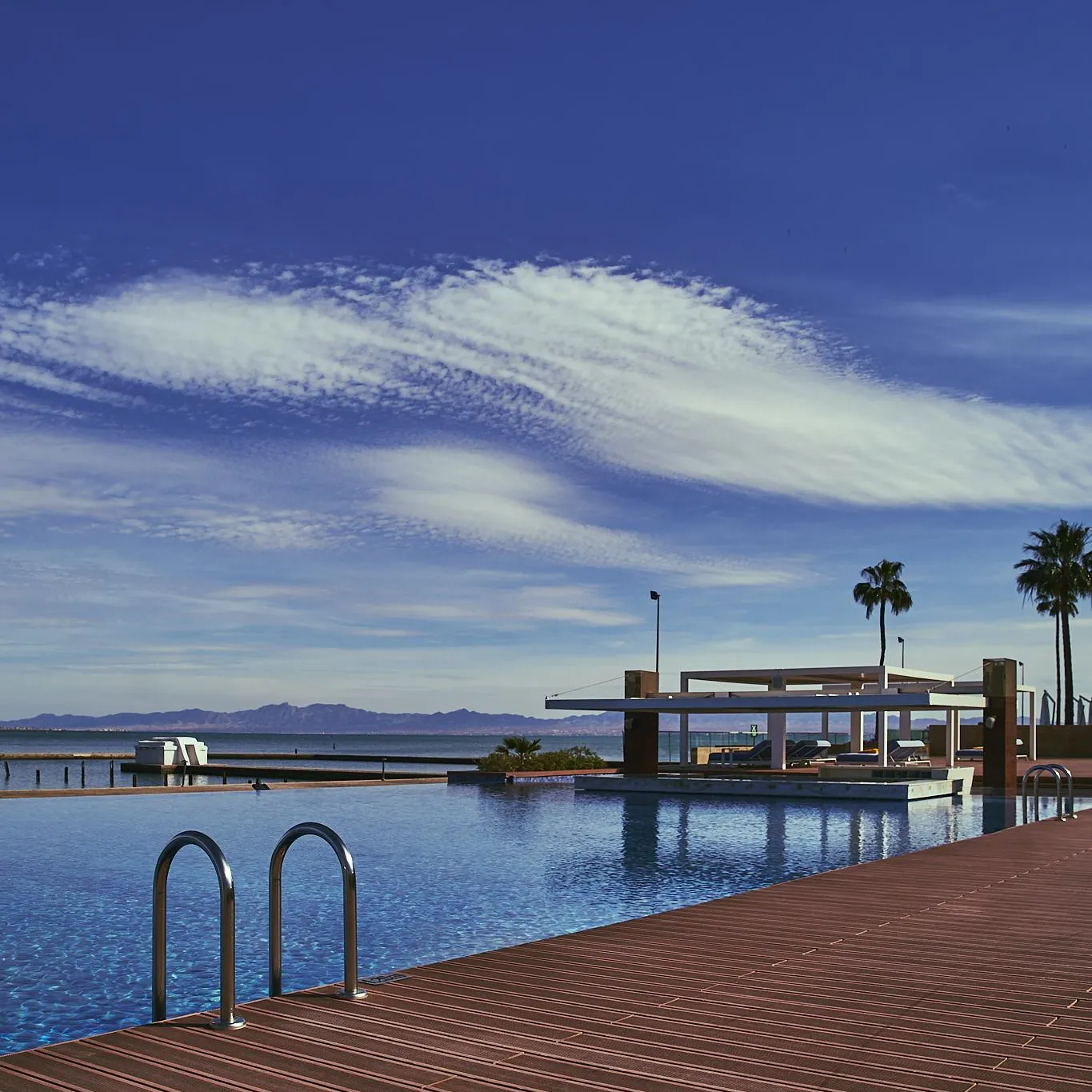 Overflow pool with a view of a lake and mountains under a blue sky with a few clouds.
