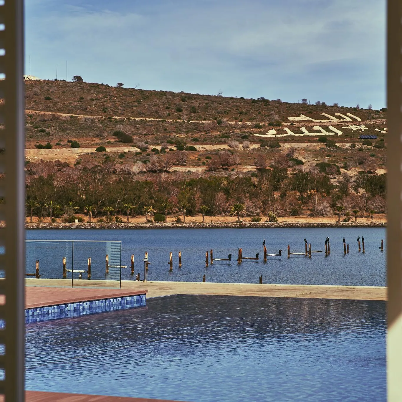 View of a lake with a pier and hills in the background, observed through shutters