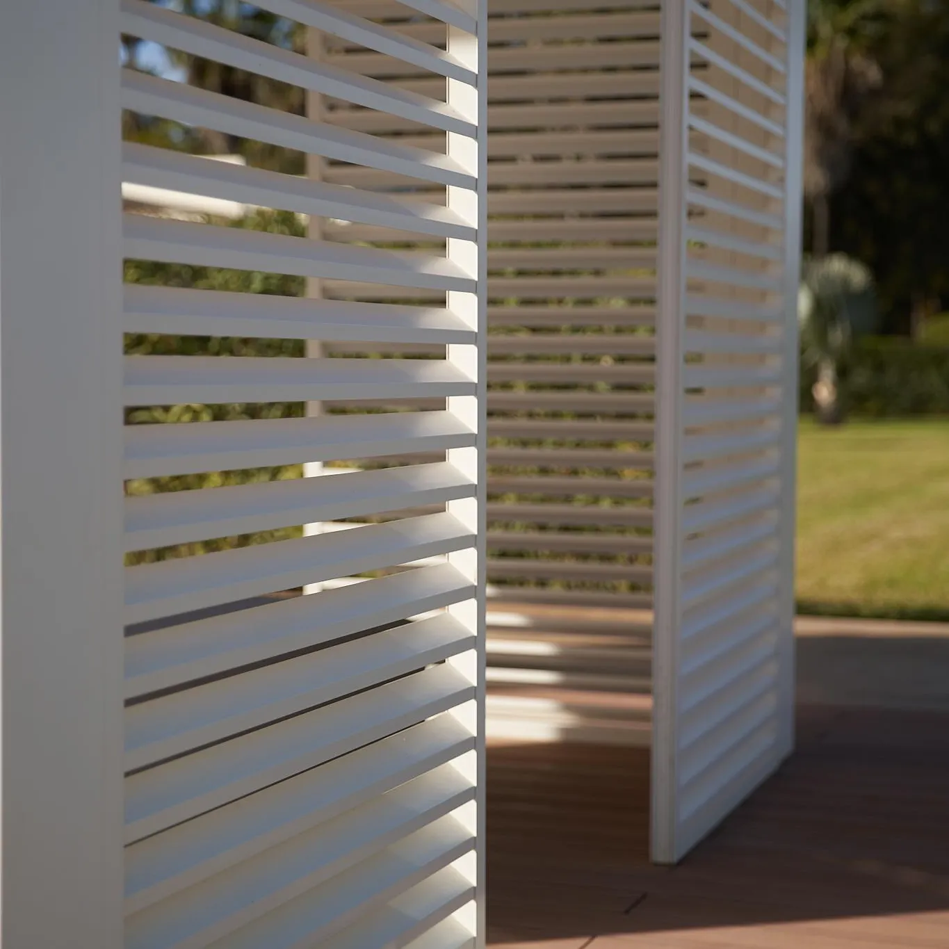 White shutters on a wooden balcony with a view of a garden and trees in the background