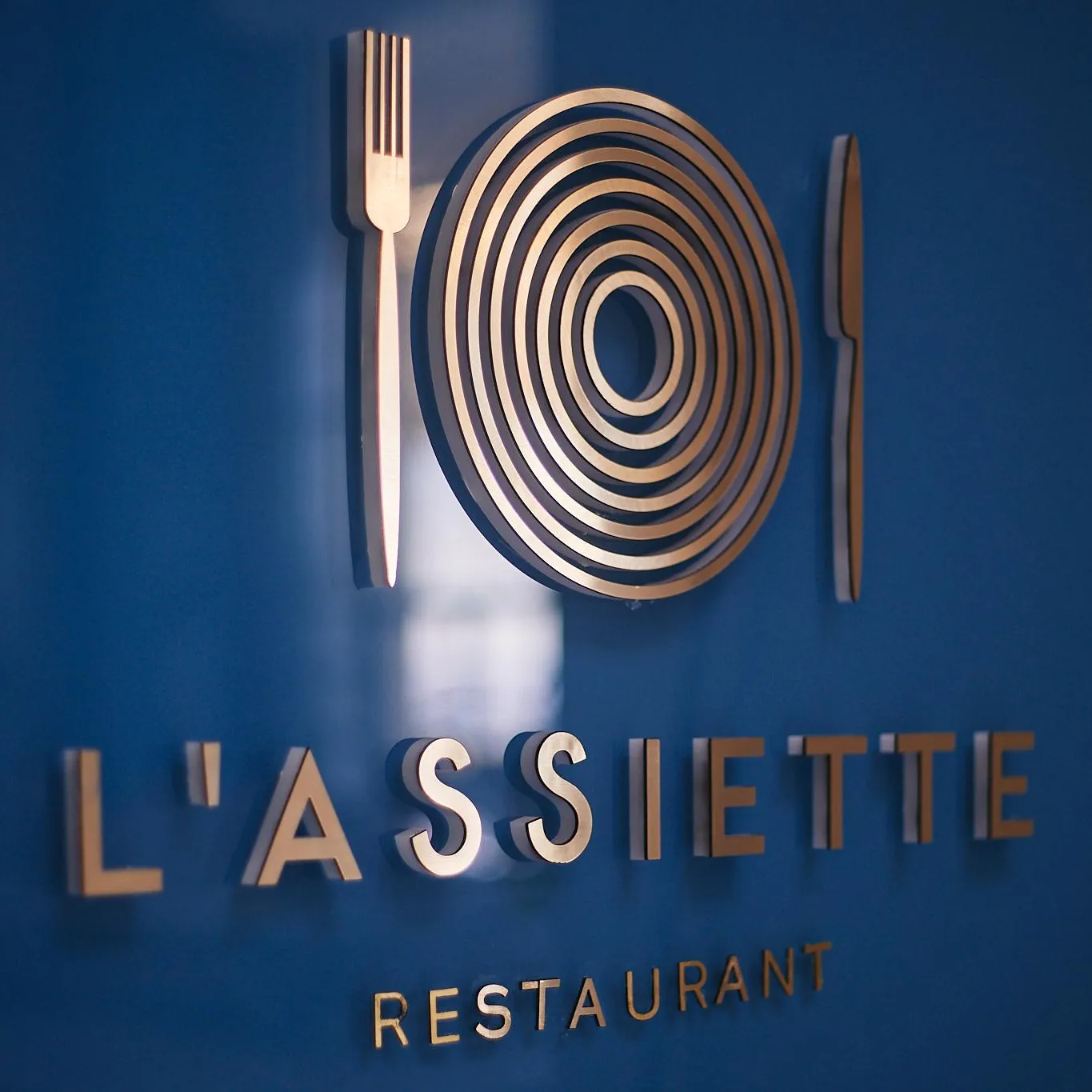 Wall plaque of a restaurant named "L'Assiette" with a logo depicting a plate between two cutlery items