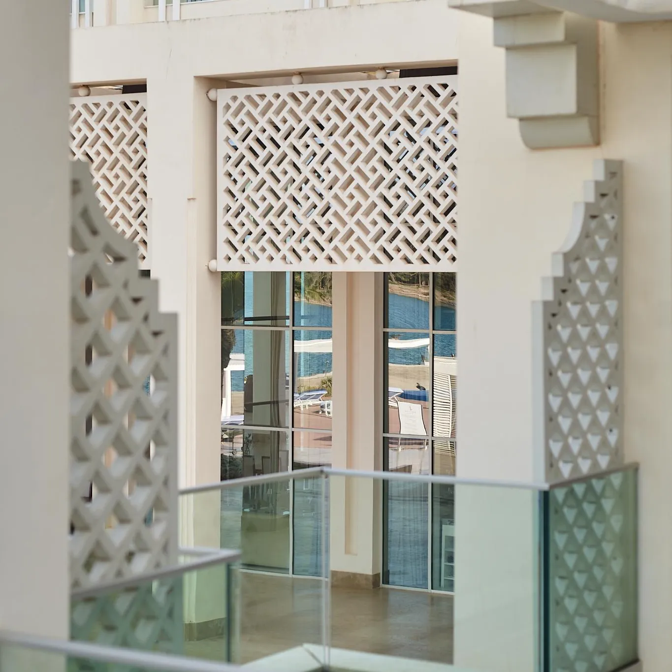Balcon with glass railing and decorative panels with geometric patterns, view of a beach and the sea in the distance.