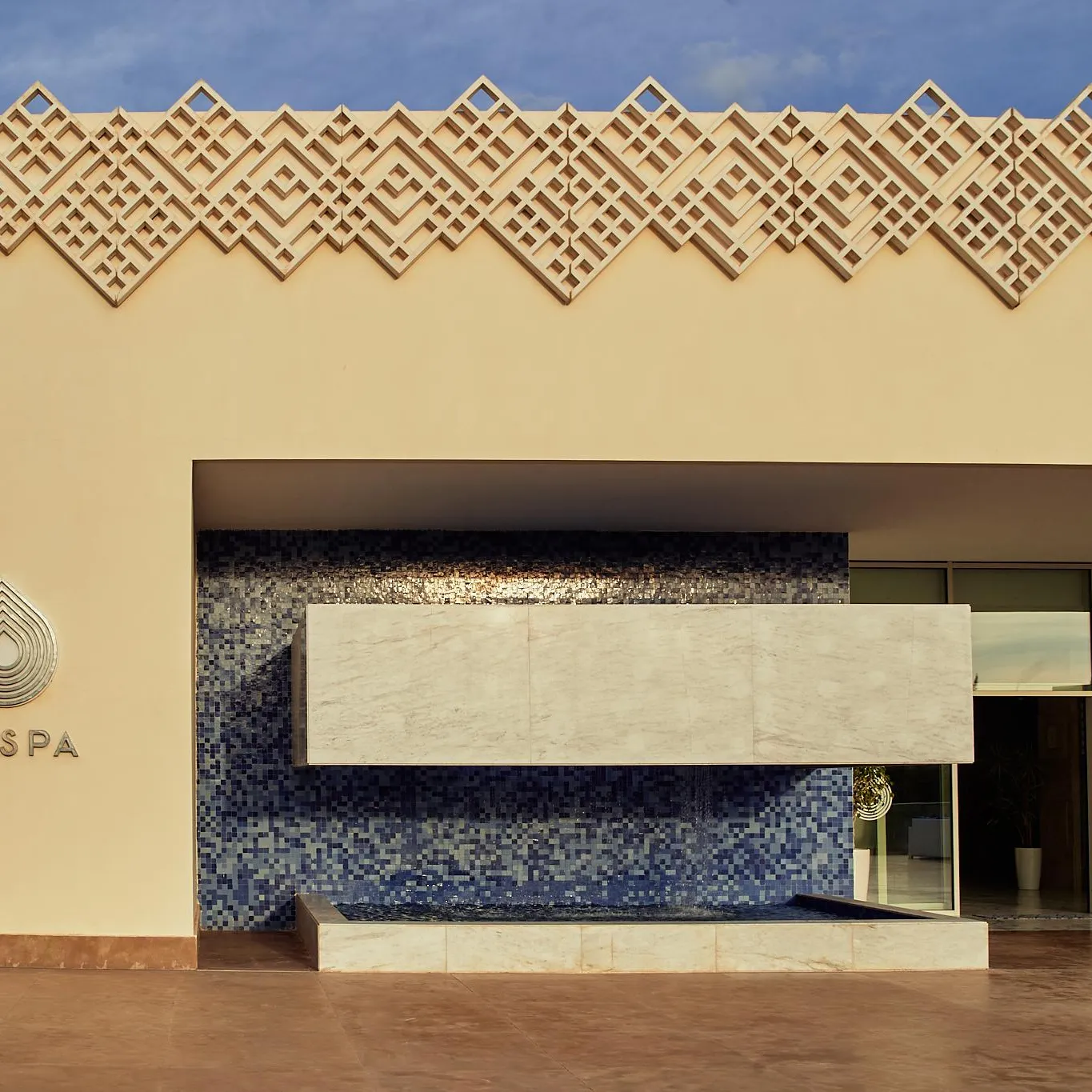 Facade of a spa with a blue mosaic wall, a stone table, and potted plants