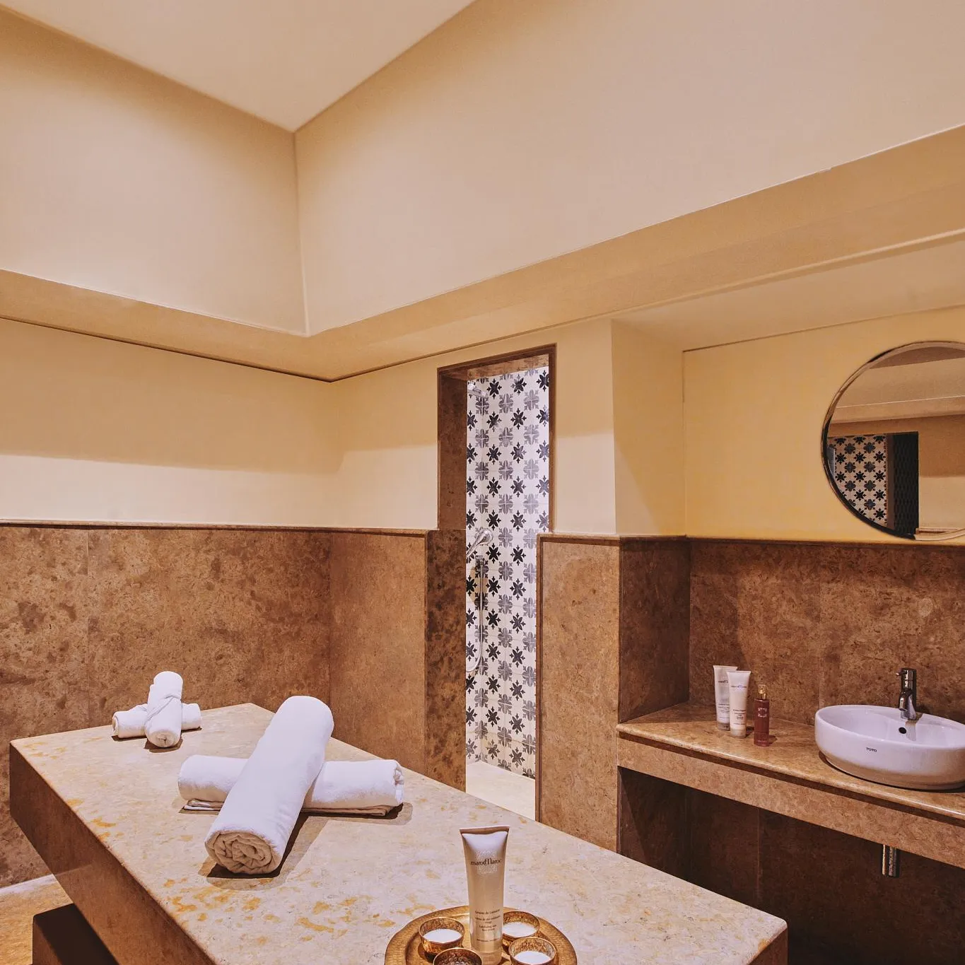 Massage room with treatment table, towels, products, and sink in a setting with stone walls and dim lighting.