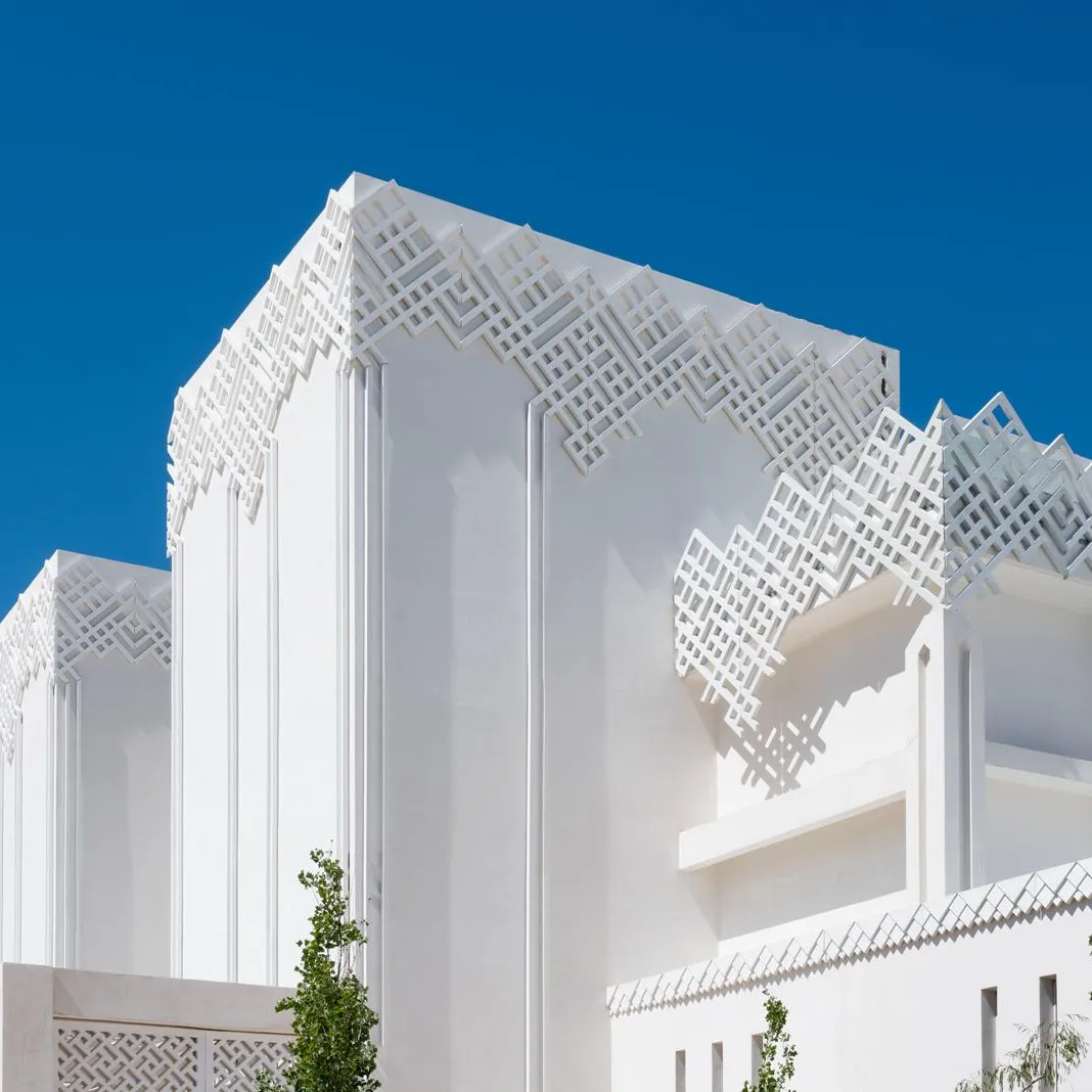 White building with geometric relief patterns on the facade and roof, under a clear blue sky