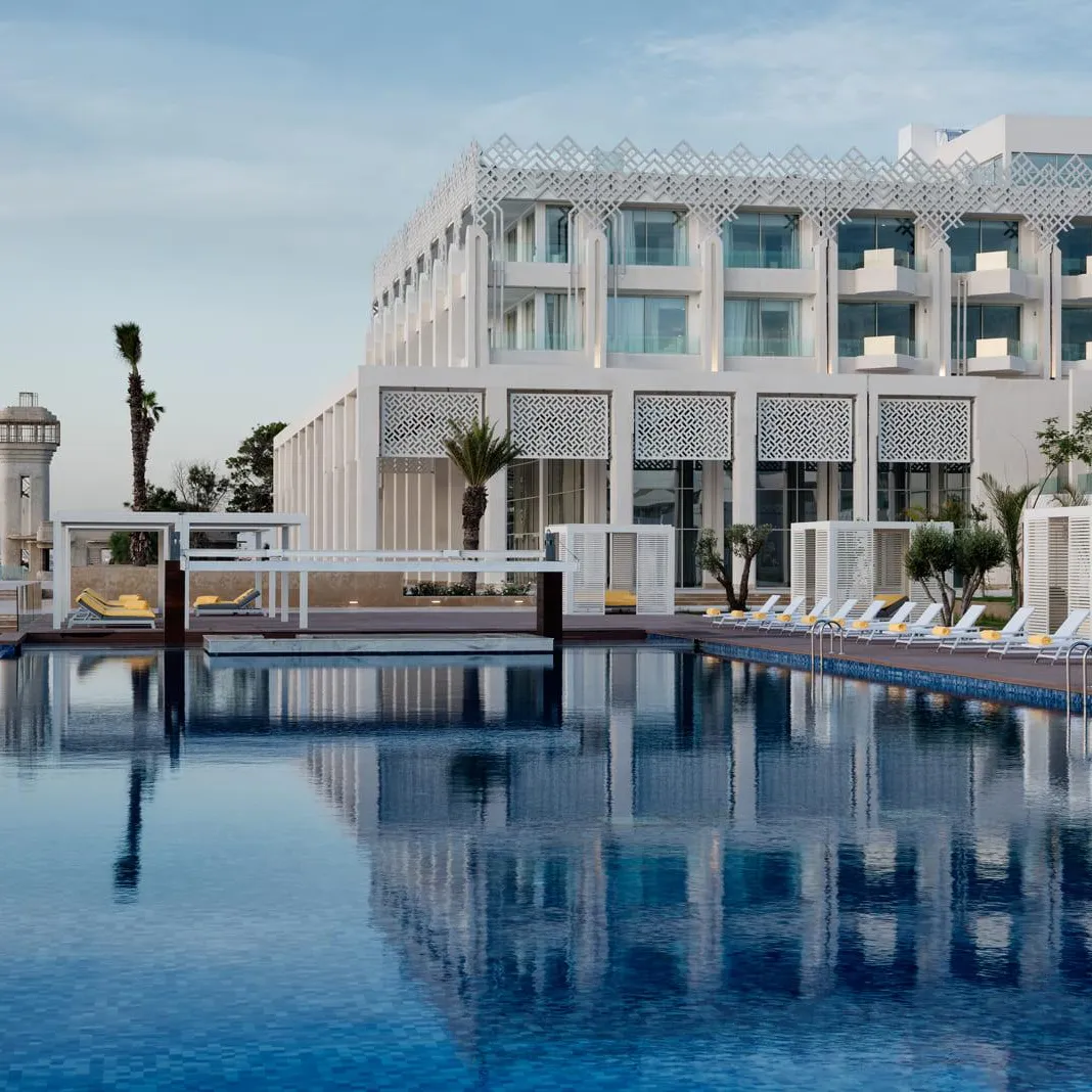 Overflow pool in front of a modern hotel with sun loungers and palm trees, sea view in the background