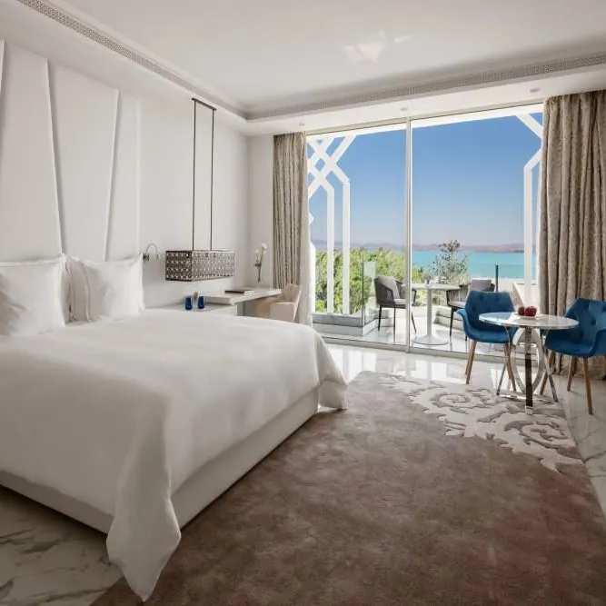 Hotel room with a double bed, table and chairs near a large window offering a sea view
