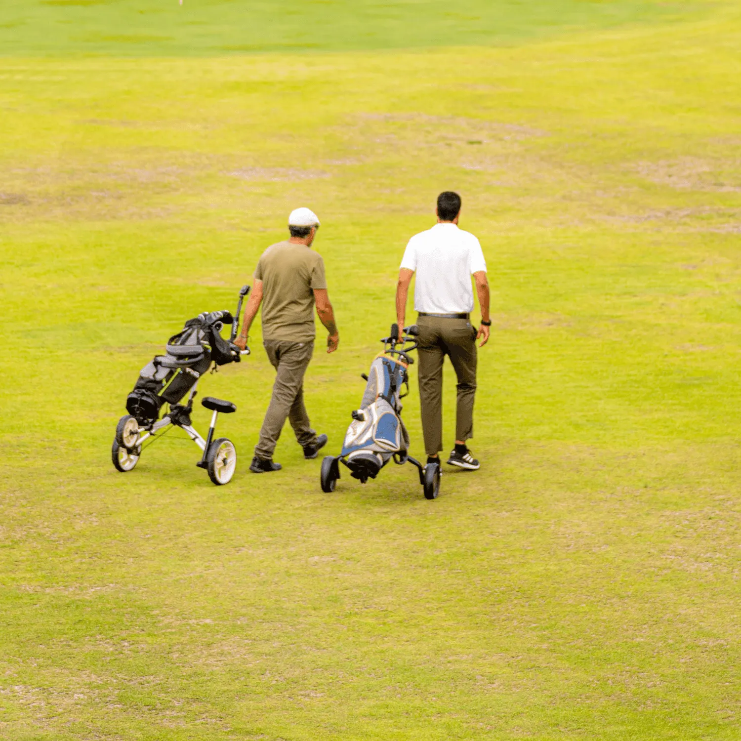 Two people are walking on a golf course pushing golf club carts.