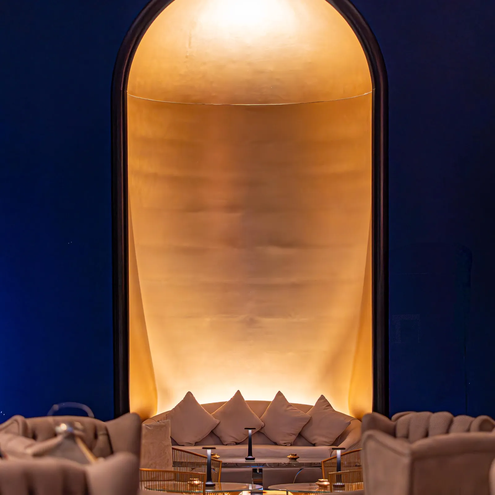 An interior space with sofas and a coffee table, lit by golden light through an arch.