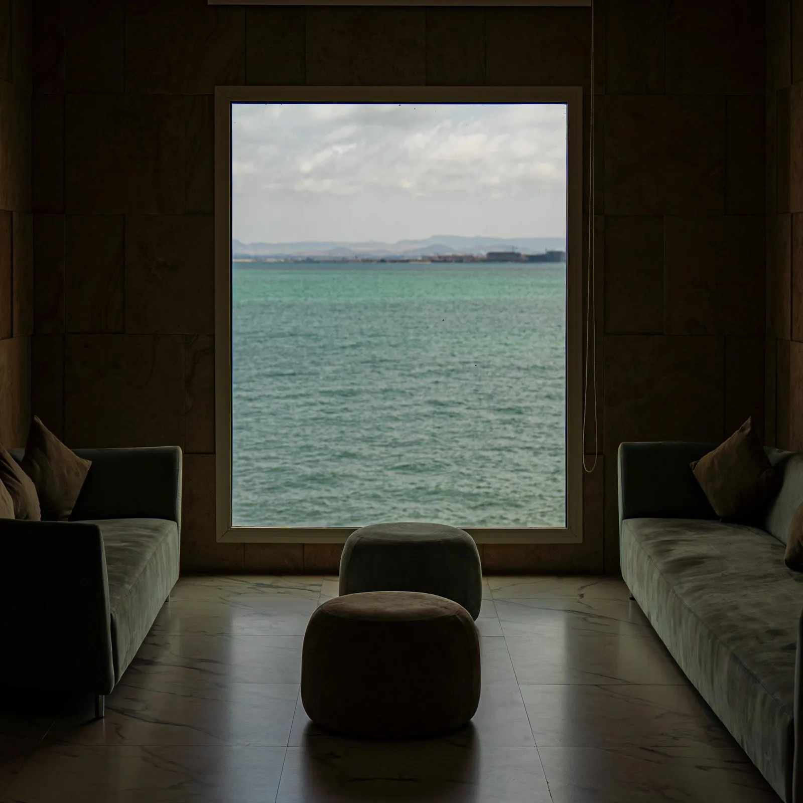 Interior room with sea view through a large window, furnished with two sofas and an ottoman