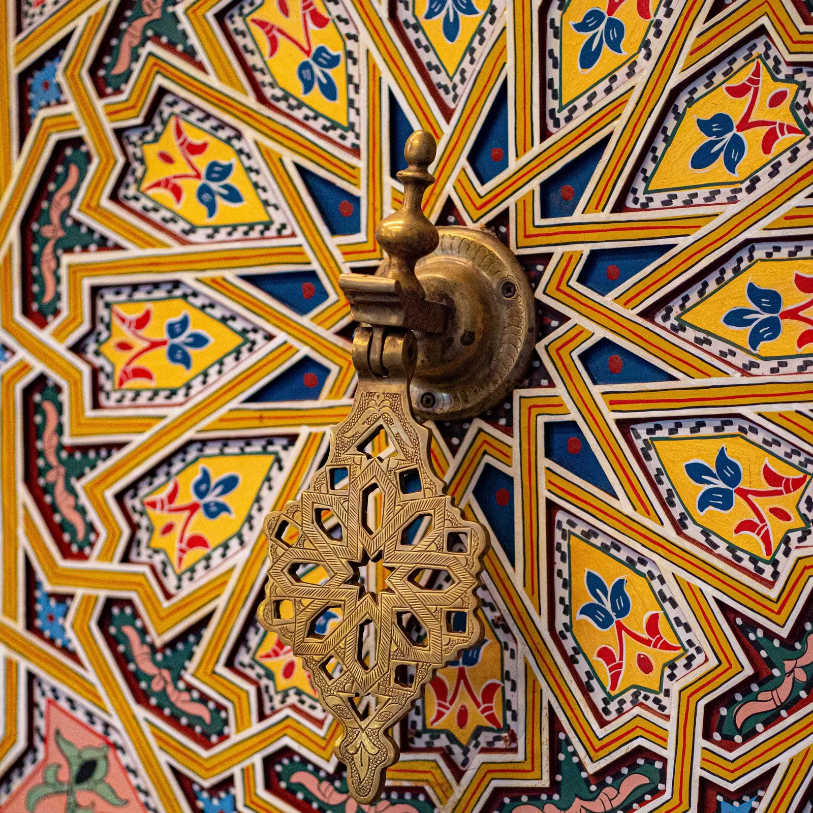 A metal candelabrum with an Ethiopian cross is suspended from a ceiling adorned with colorful geometric patterns.