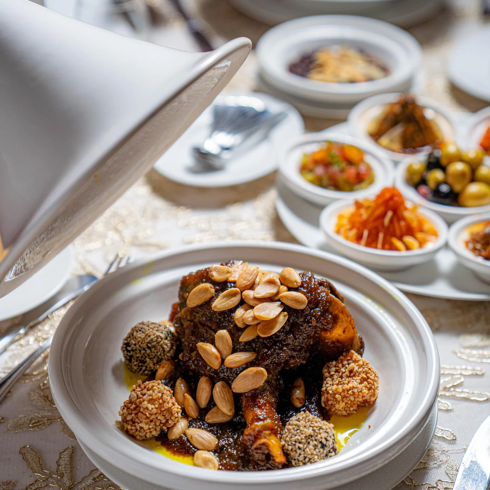 A dish of meat topped with sesame seeds and almonds, surrounded by several small bowls of various culinary preparations.