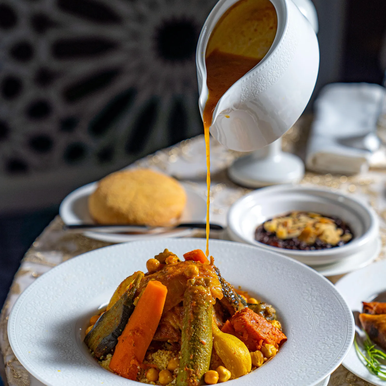 A hand pours sauce from a ladle onto a dish containing vegetables and chickpeas.