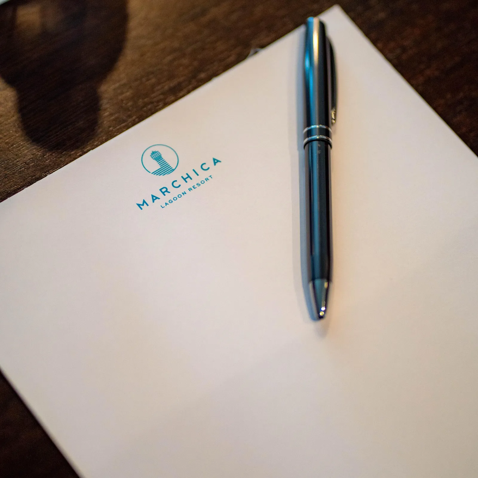A sheet of paper with the logo "Marchica Lagoon Resort" and a pen placed on it on a wooden table