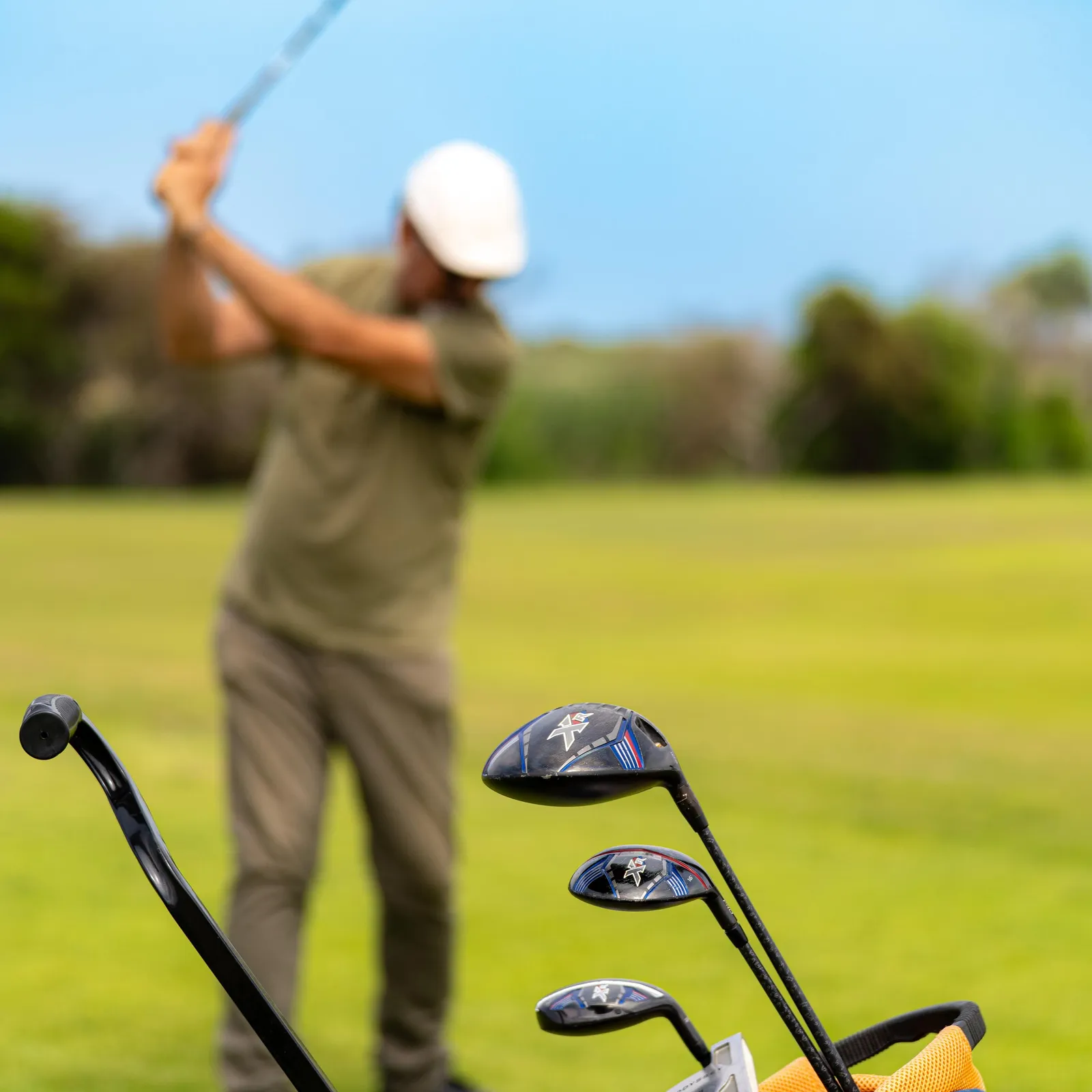 A golfer in action on a green with a bag of clubs nearby