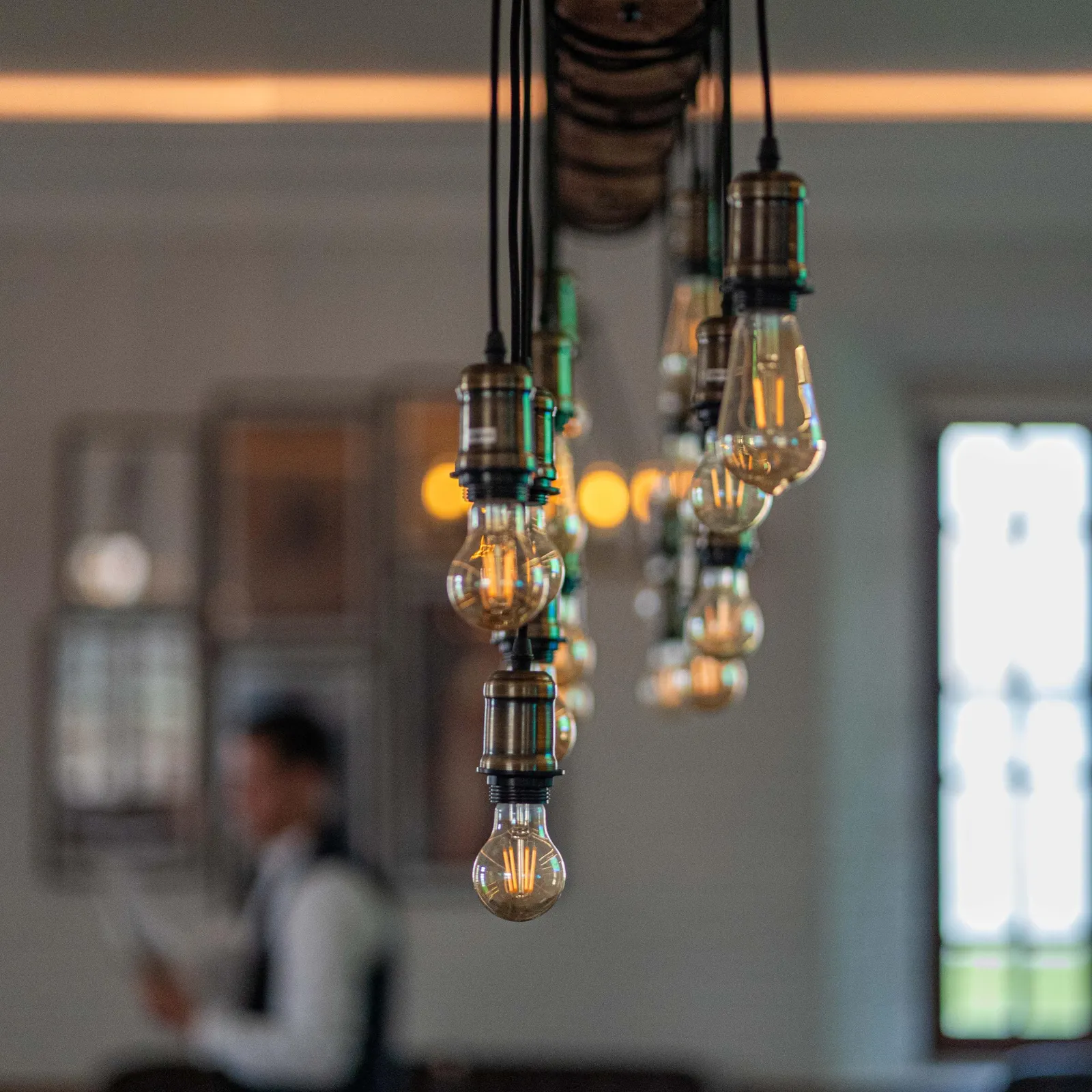A pendant light fixture with multiple lit bulbs in a blurred interior