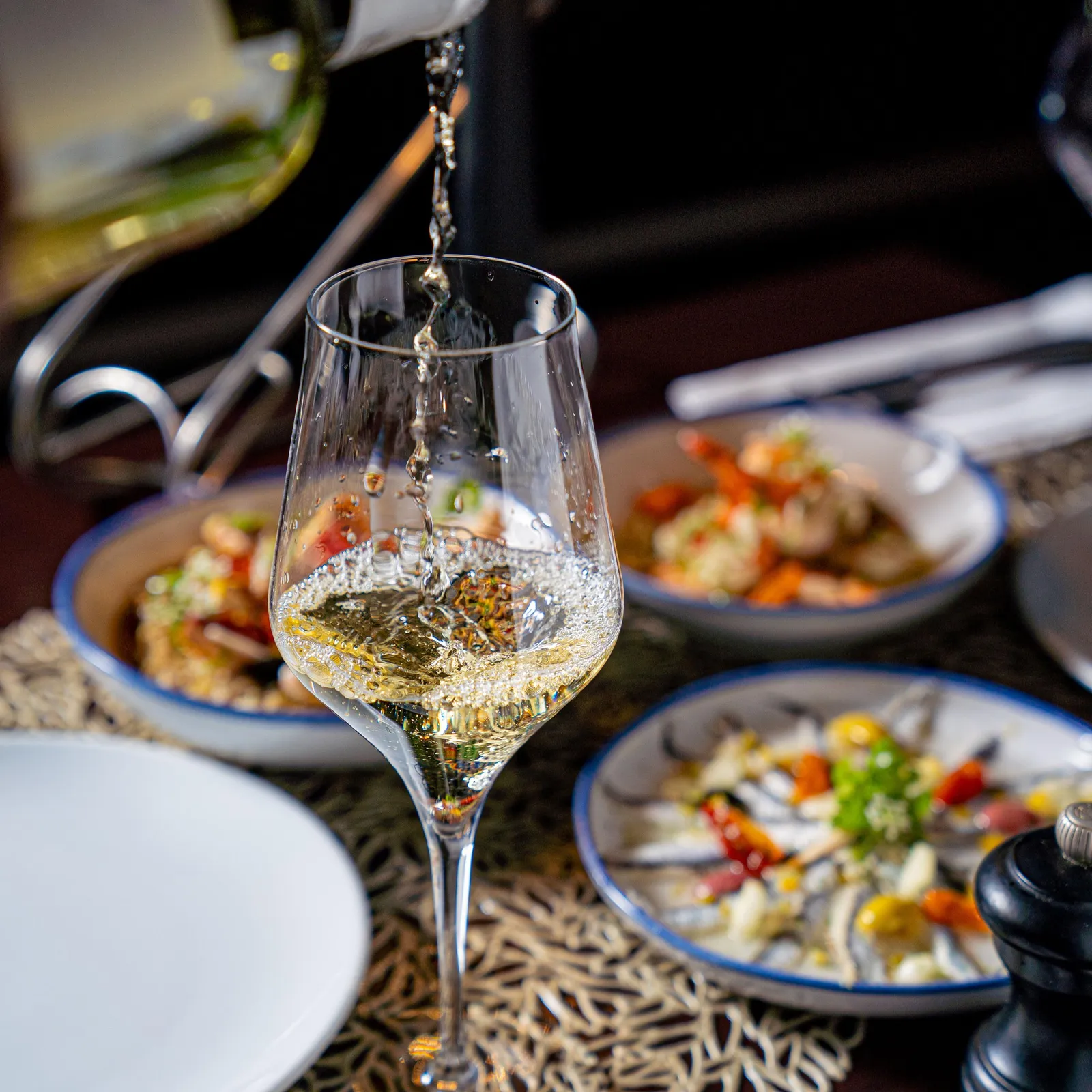 A wine glass is filled with white wine, with salad plates and cutlery on a table.