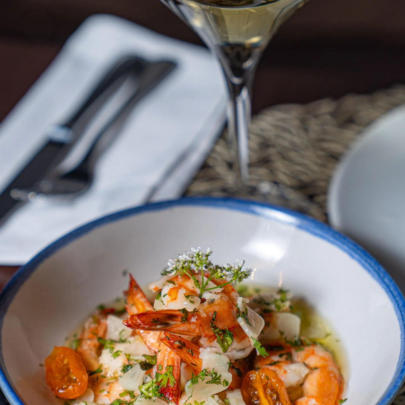 A bowl of grilled shrimp with cherry tomatoes and onions, served with a glass of white wine
