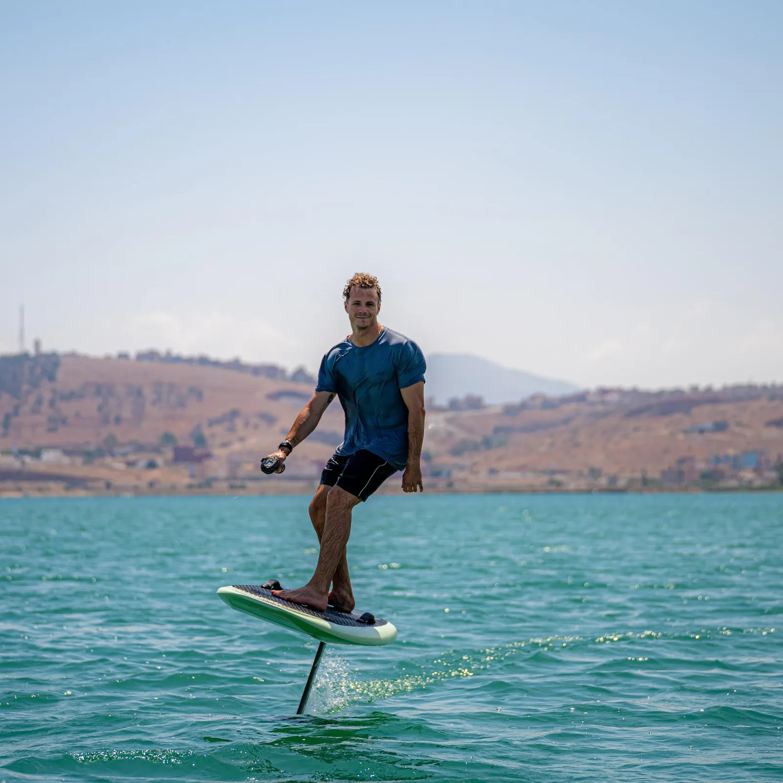 A man standing on a paddleboard in a body of water with hills in the background.