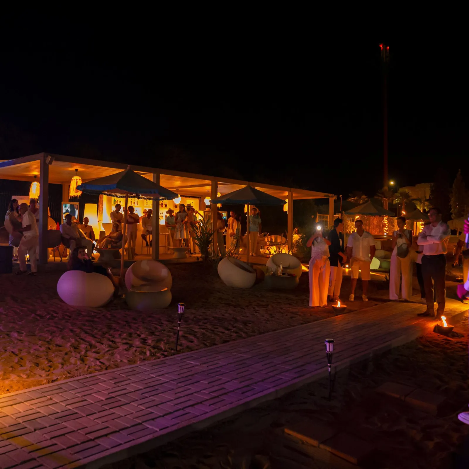 A group of people stands around a lit structure on a nighttime beach.