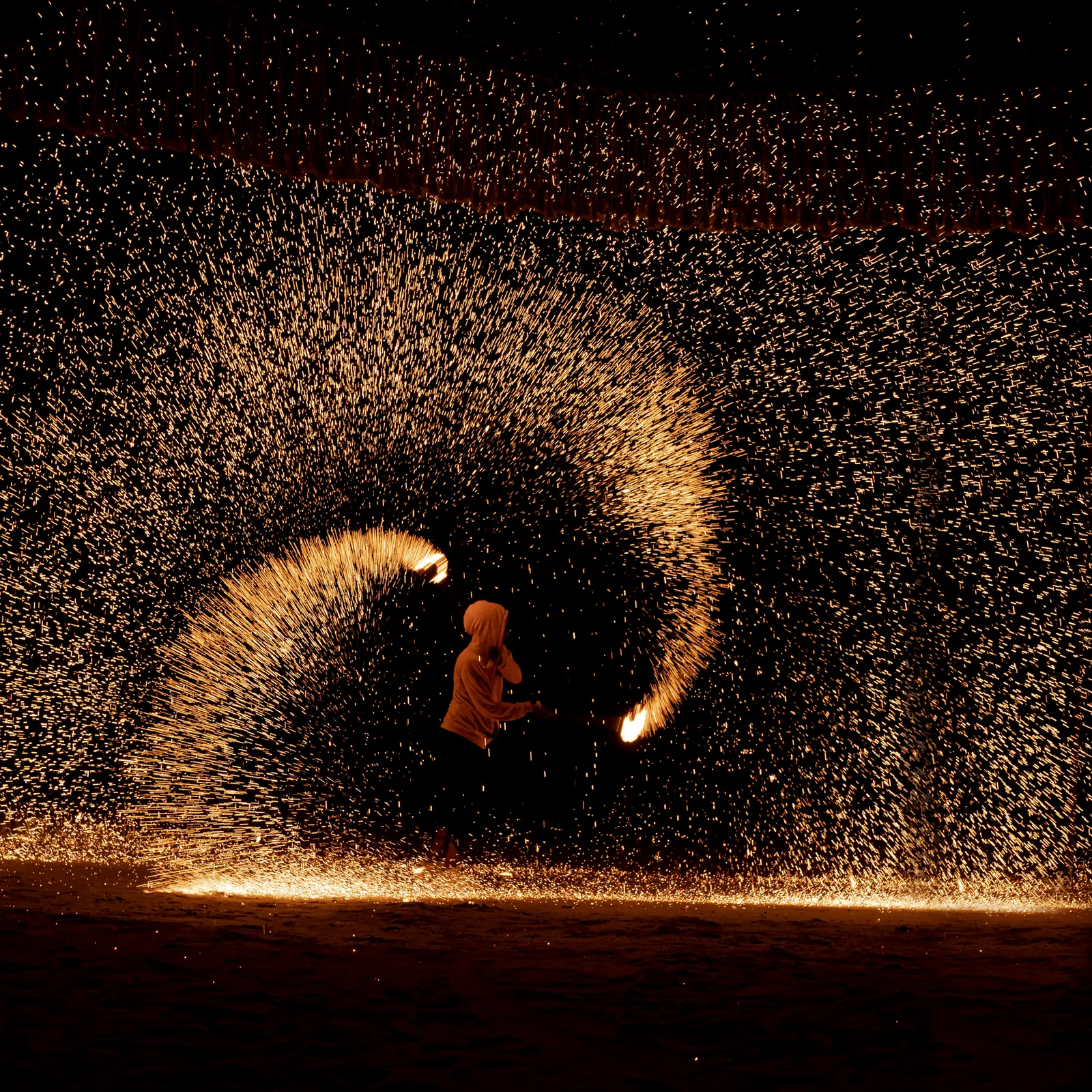 A person throws sparks in an arc on a nighttime beach.