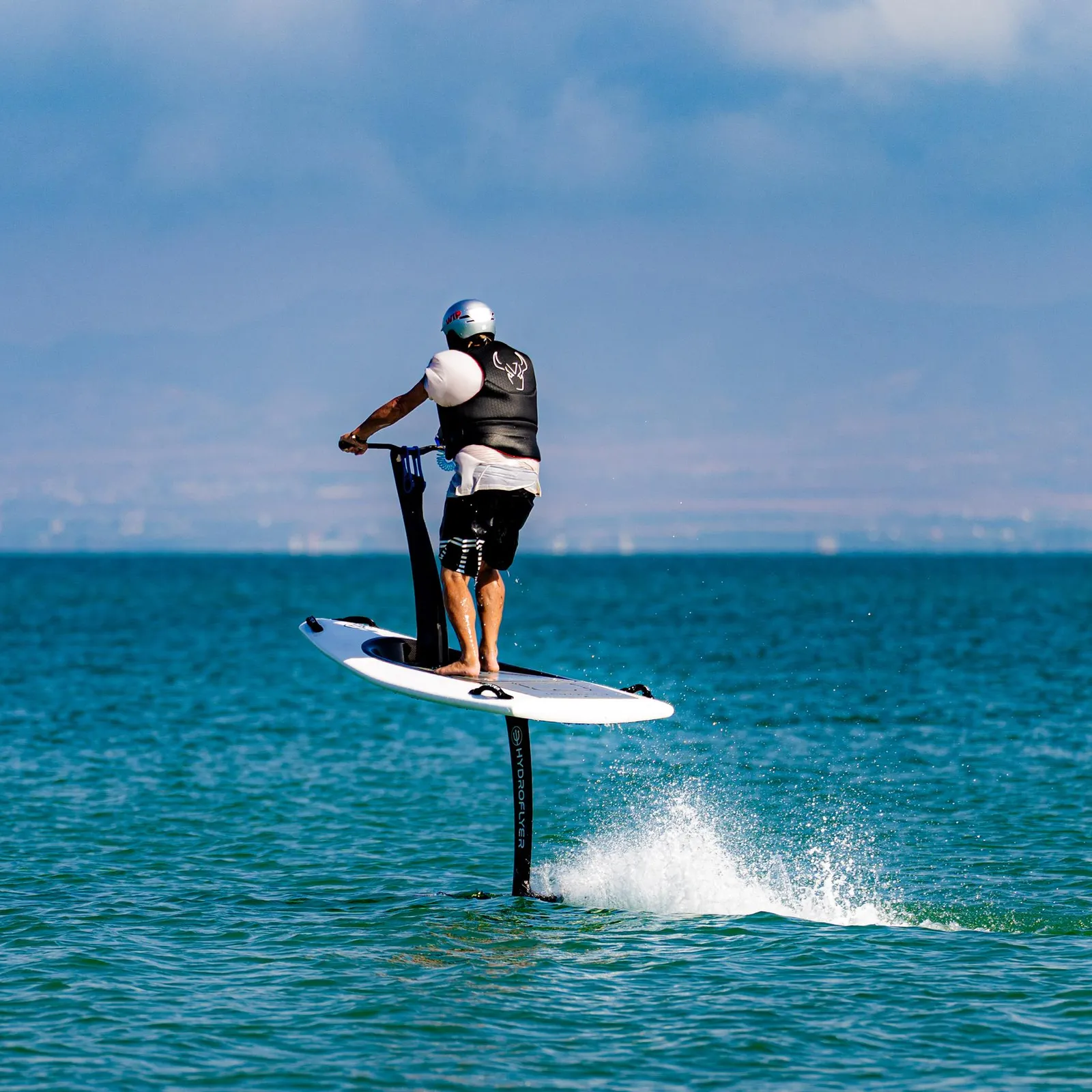 A man on an electric paddleboard moves forward on the water with a jet of water behind him.