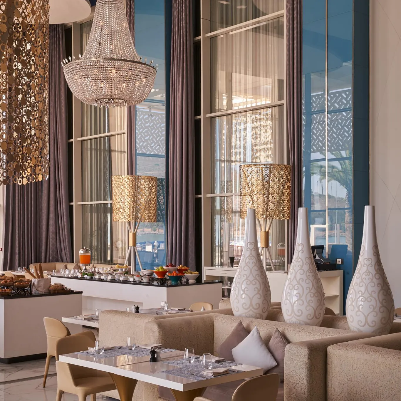 Elegant dining room with tables, chairs, sofas, chandeliers and sea view through large windows