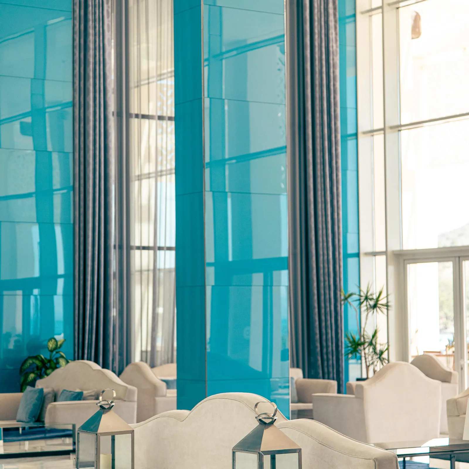A modern living room with white sofas, lanterns on a coffee table, and large blue windows