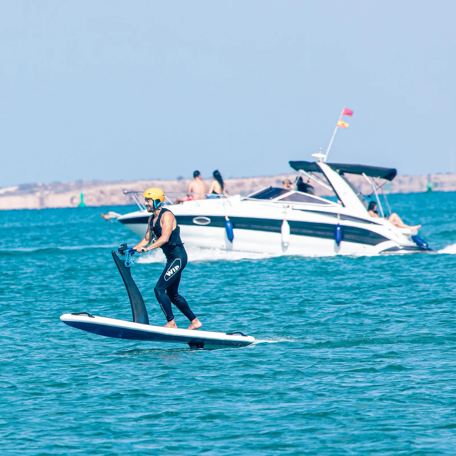 A person is paddleboarding with a paddle in the sea, a boat is visible in the background.