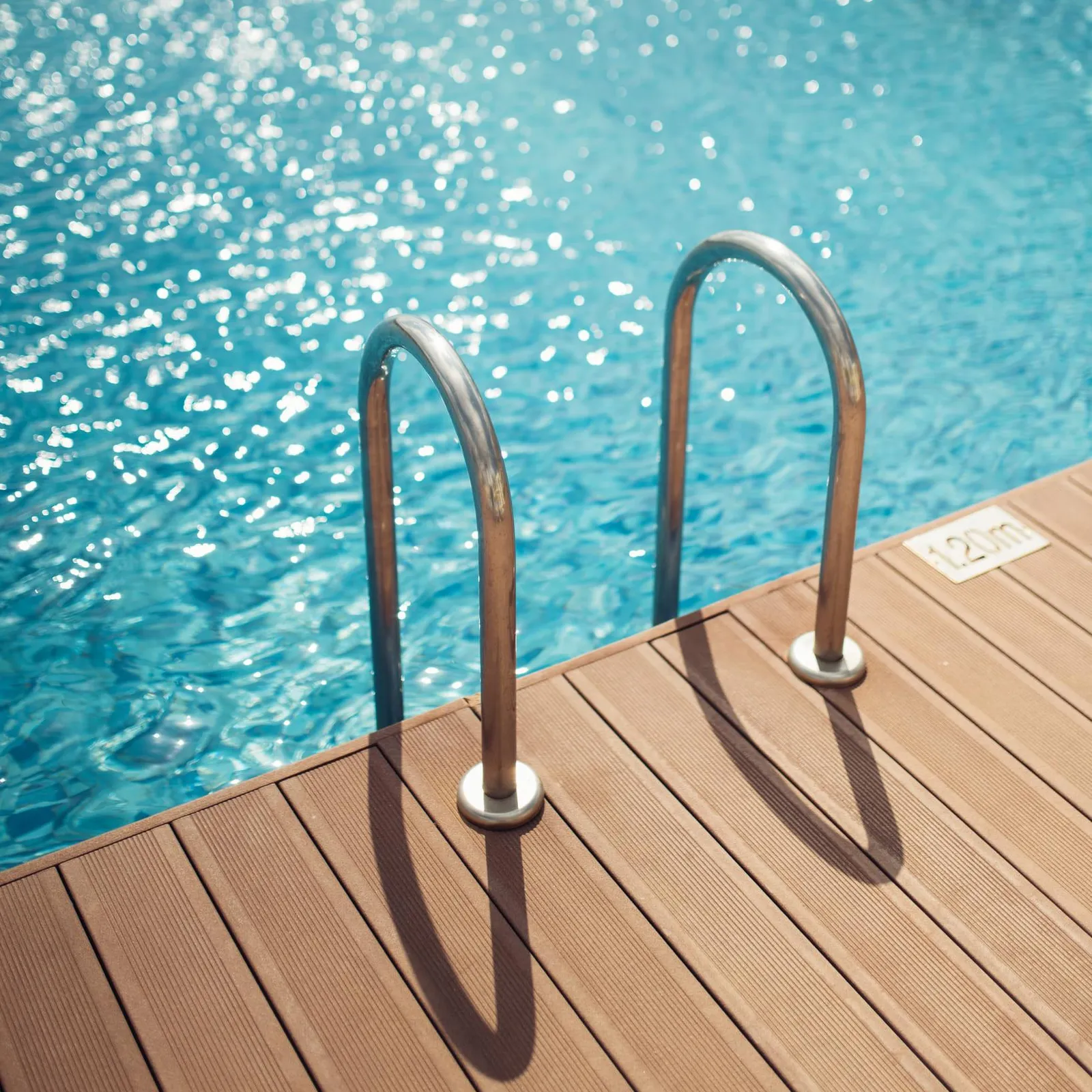 Two curved metal bars attached to a wooden floor near a pool filled with blue water