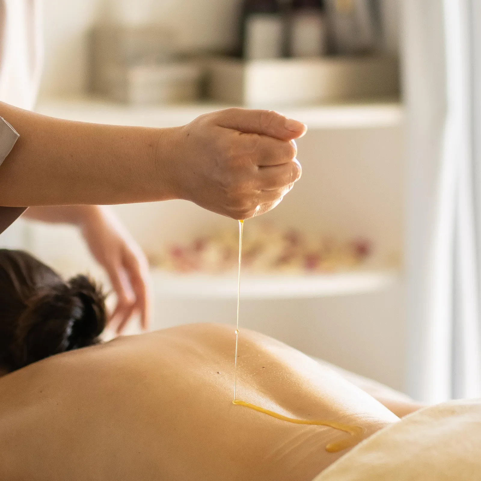A person pours a liquid onto the back of a person lying on a massage table.
