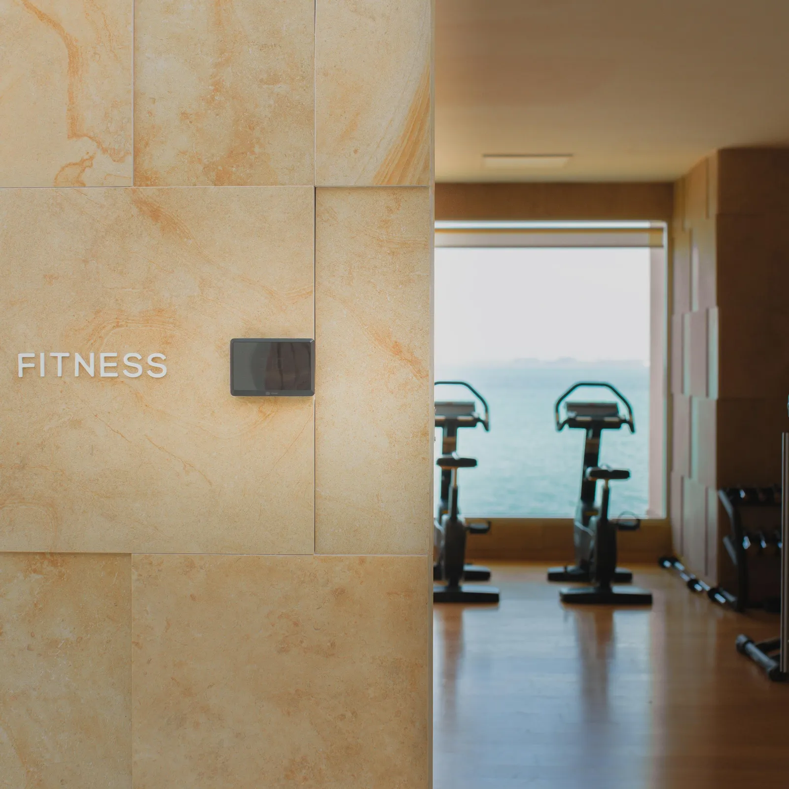 View of a fitness space with exercise bikes, visible through an open door, and a stone wall with the inscription "FITNESS"
