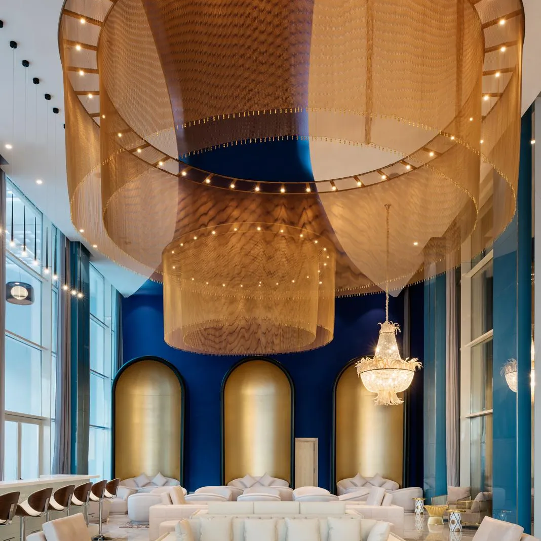 A luxurious lounge with white sofas, coffee tables, and a ceiling decorated with golden fabrics and lights.
