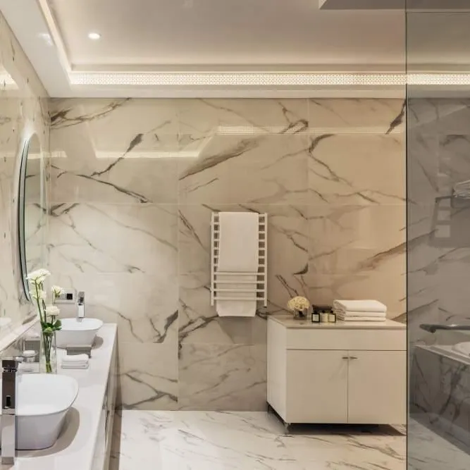 Modern bathroom with double sink, round mirror, glass shower, and beige marble walls