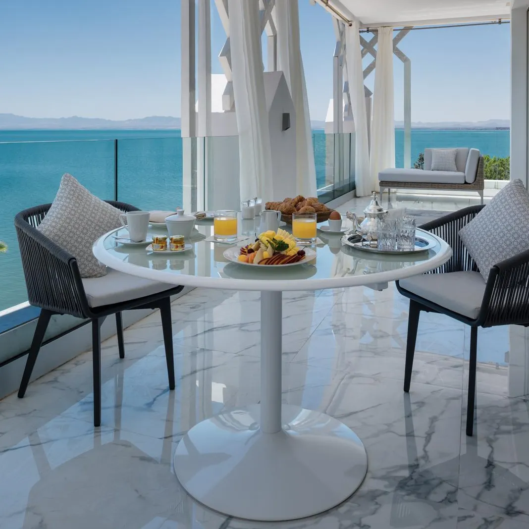 A table with breakfast is set up on a balcony with a sea view.