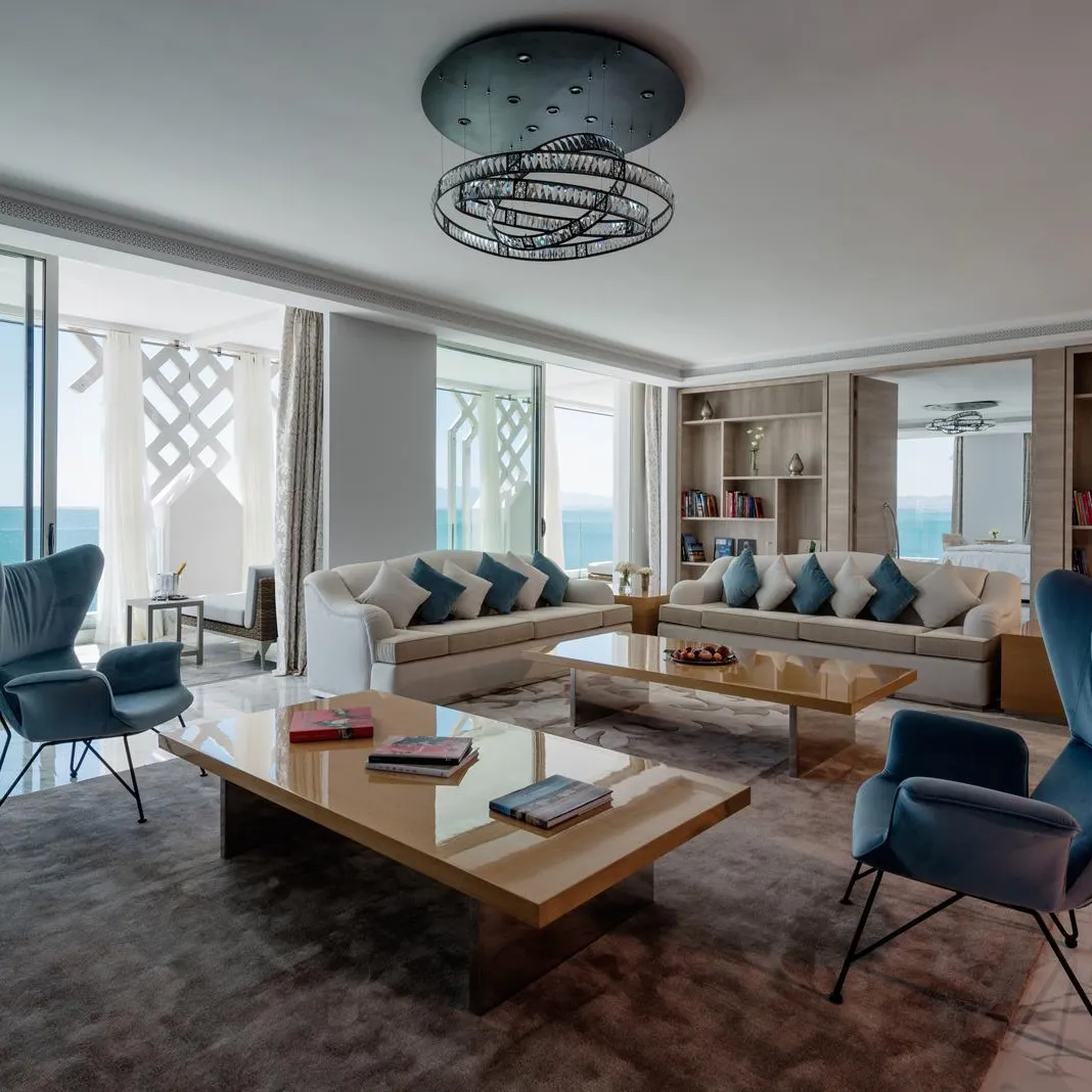 Modern living room with sea view, featuring a sofa, armchairs, a coffee table and shelves filled with books.