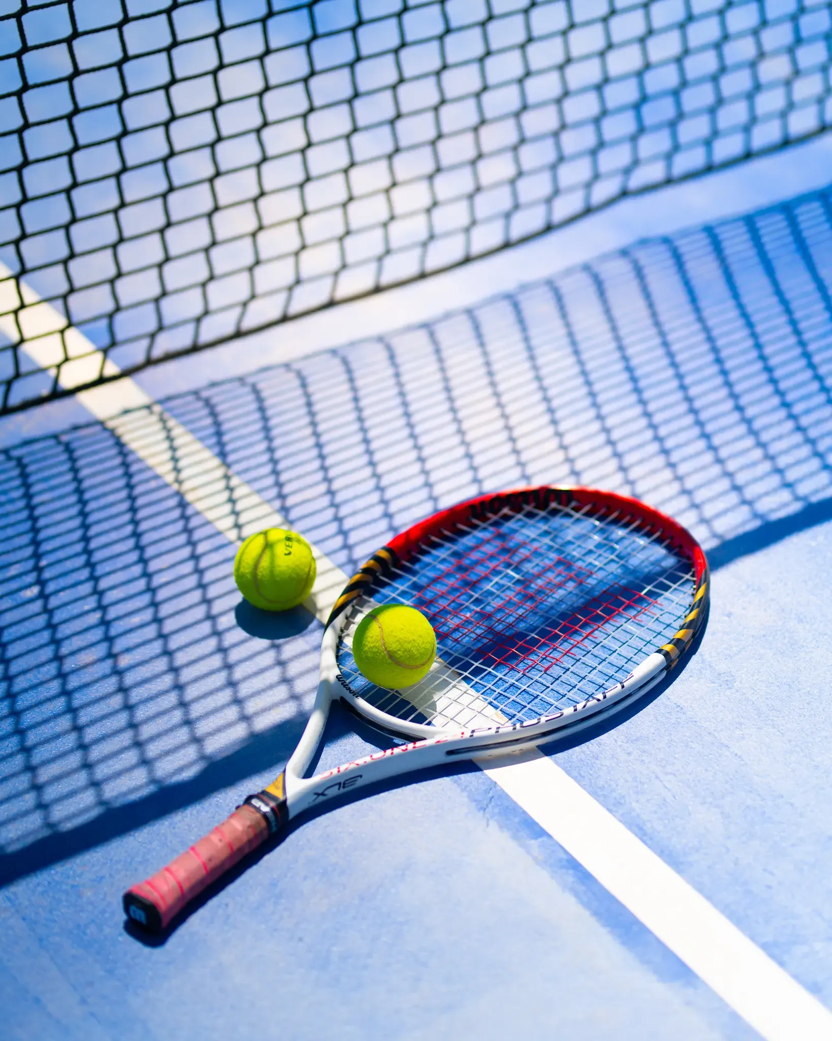 Raqueta de tenis con dos pelotas sobre una pista cerca de la red