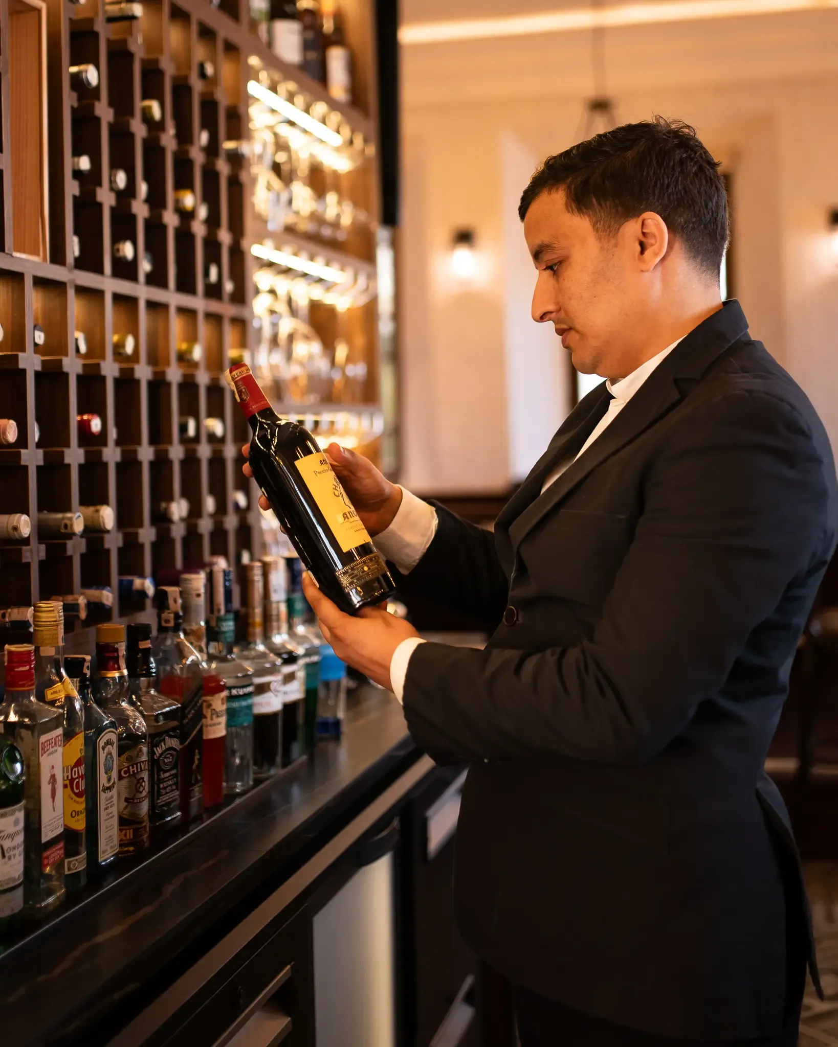 Un homme en costume examine une bouteille de vin derrière un bar bien approvisionné
