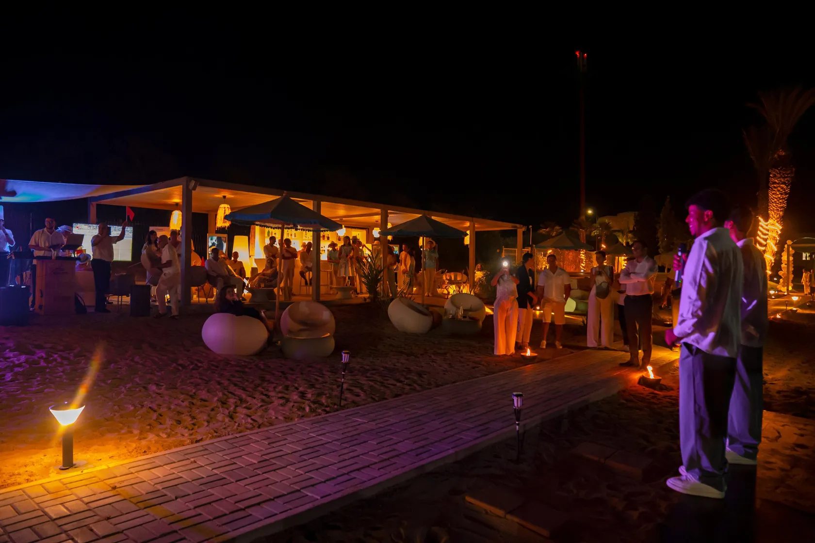 Un grupo de personas se congrega alrededor de una estructura iluminada en una playa de noche