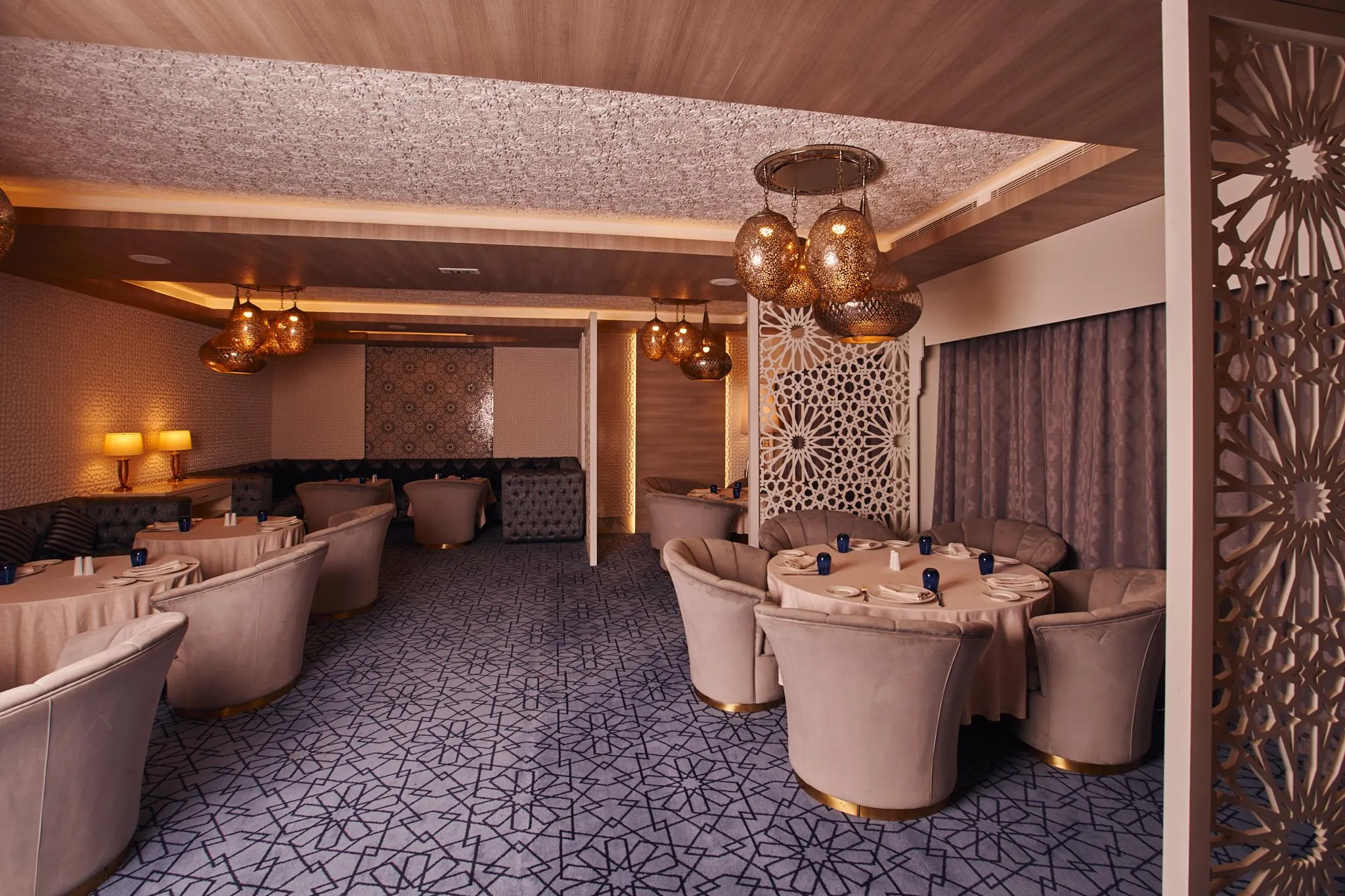 Sala de restaurante elegante con mesas redondas, sillas acolchadas de terciopelo rosa y lámparas colgantes