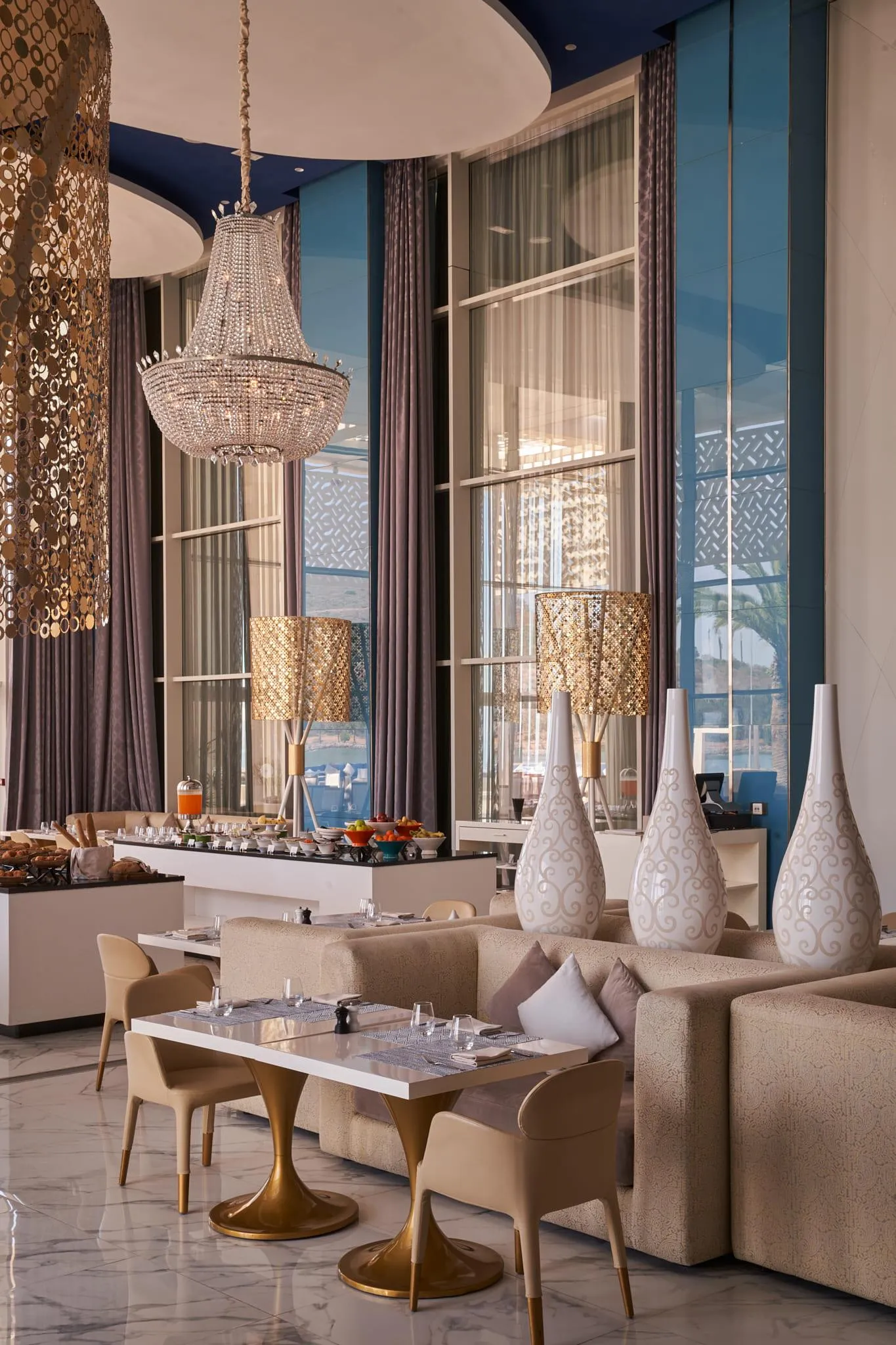 Elegant dining room with tables, chairs, sofas, chandeliers and sea view through large windows