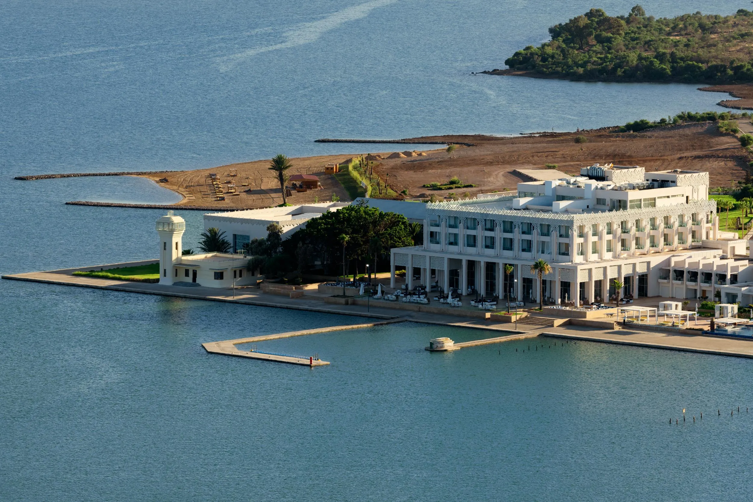 Un hôtel blanc en bord de mer avec une jetée et des tables de restaurant en terrasse