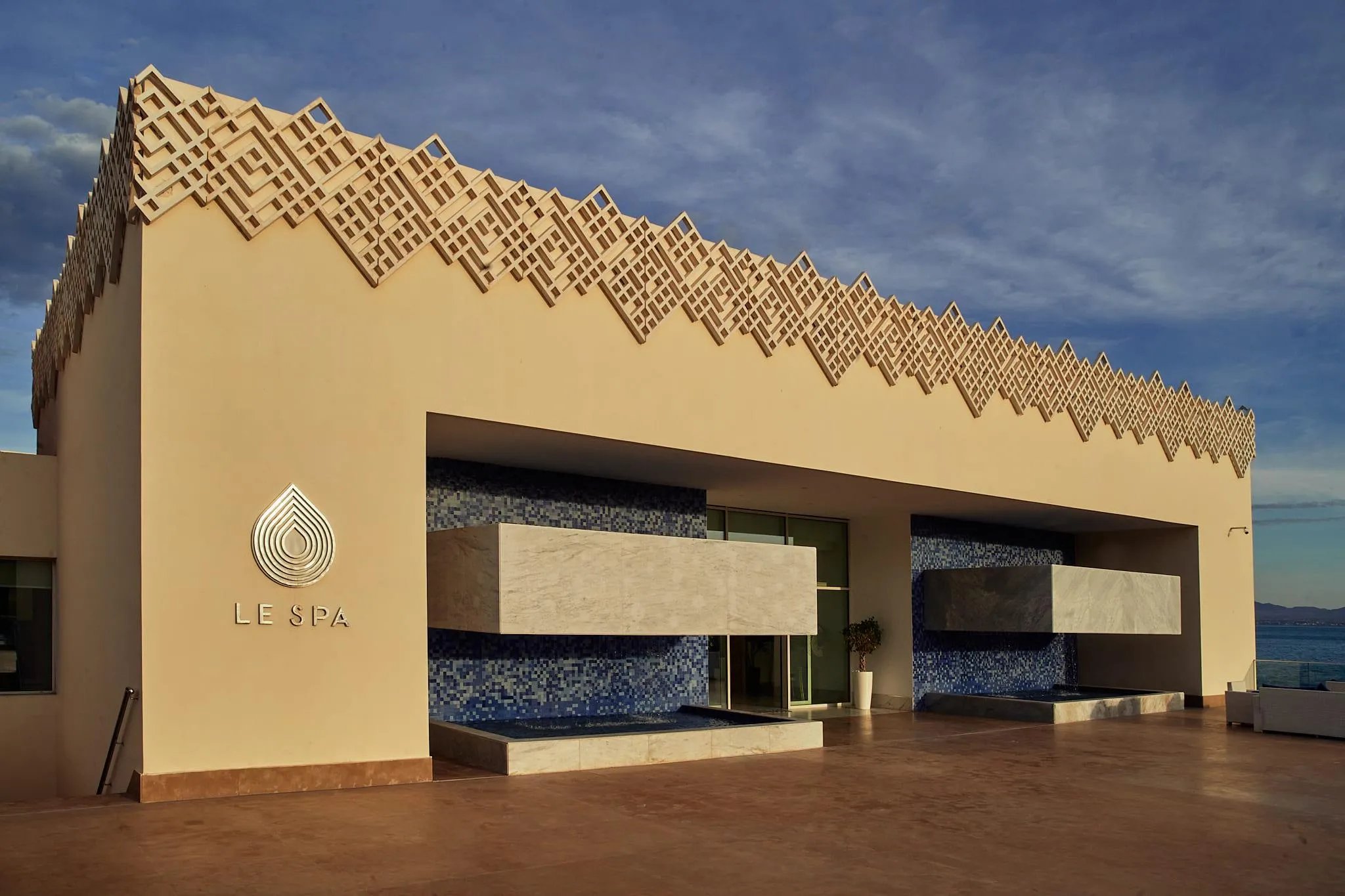 Facade of a building named "LE SPA" with a blue mosaic wall decoration and geometric relief patterns on the roof